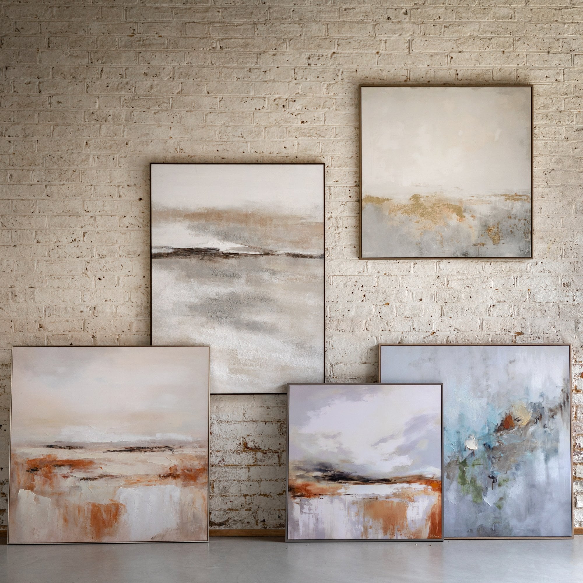 Collection of abstract paintings on a white brick wall.