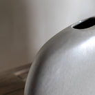 A close up of the top of a light grey vase, showcasing its smooth, rounded design.