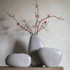 Three light grey, stone-like decorative vases of varying shapes and sizes, with flowers.