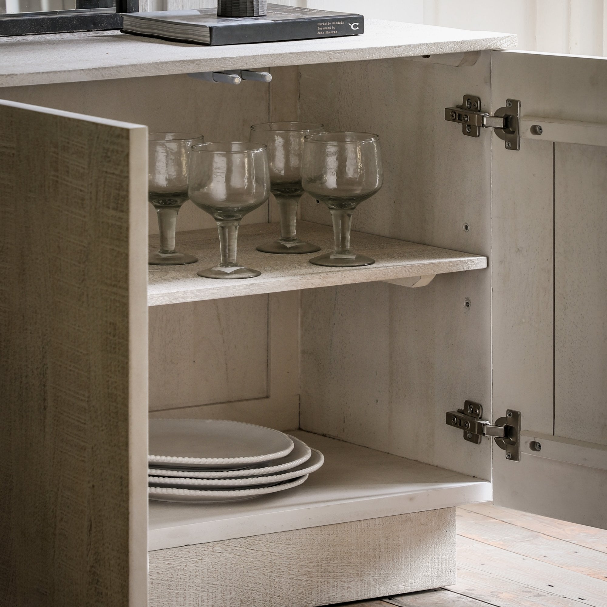 Inside a rustic wooden cabinet, revealing shelves with elegant glassware and ceramic plates.