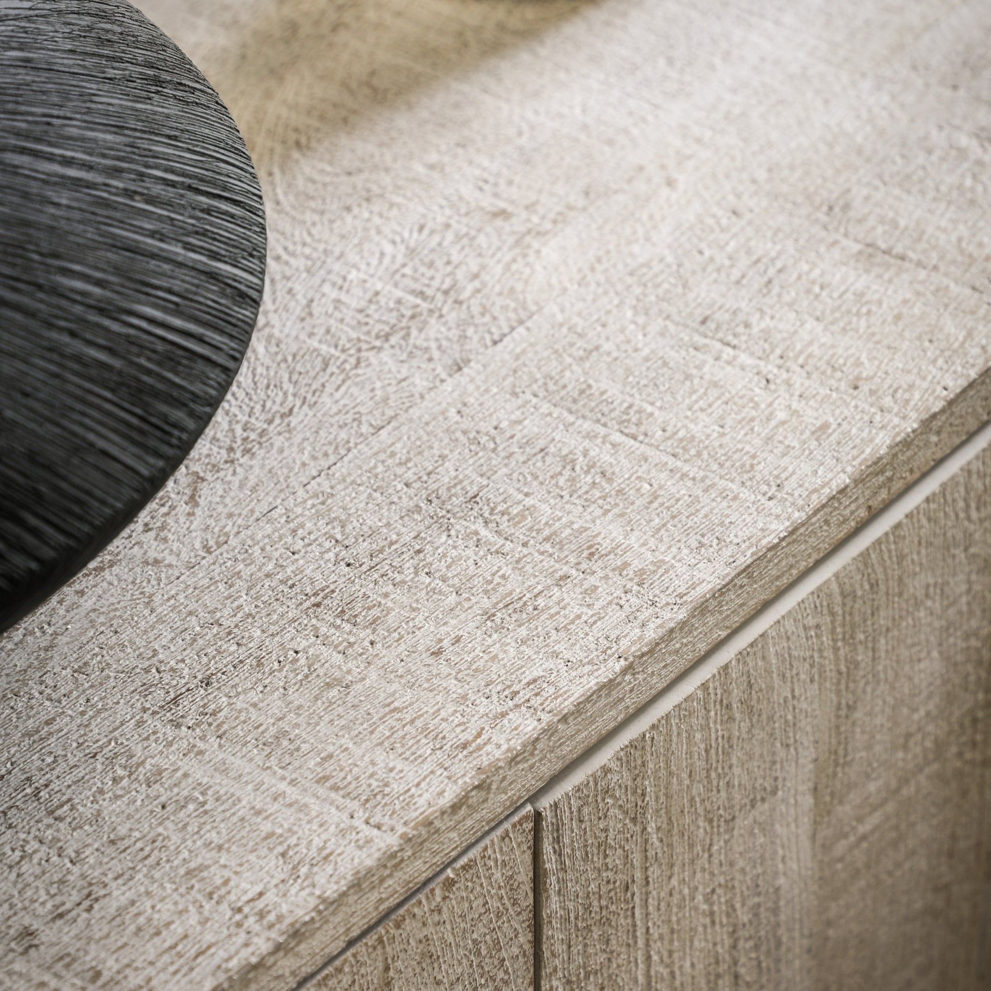 A close-up of a weathered wood surface, showcasing a unique textured black vase.