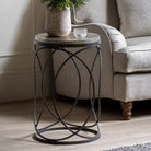 Round side table with a hammered metal top and black metal geometric base next to a gray sofa.