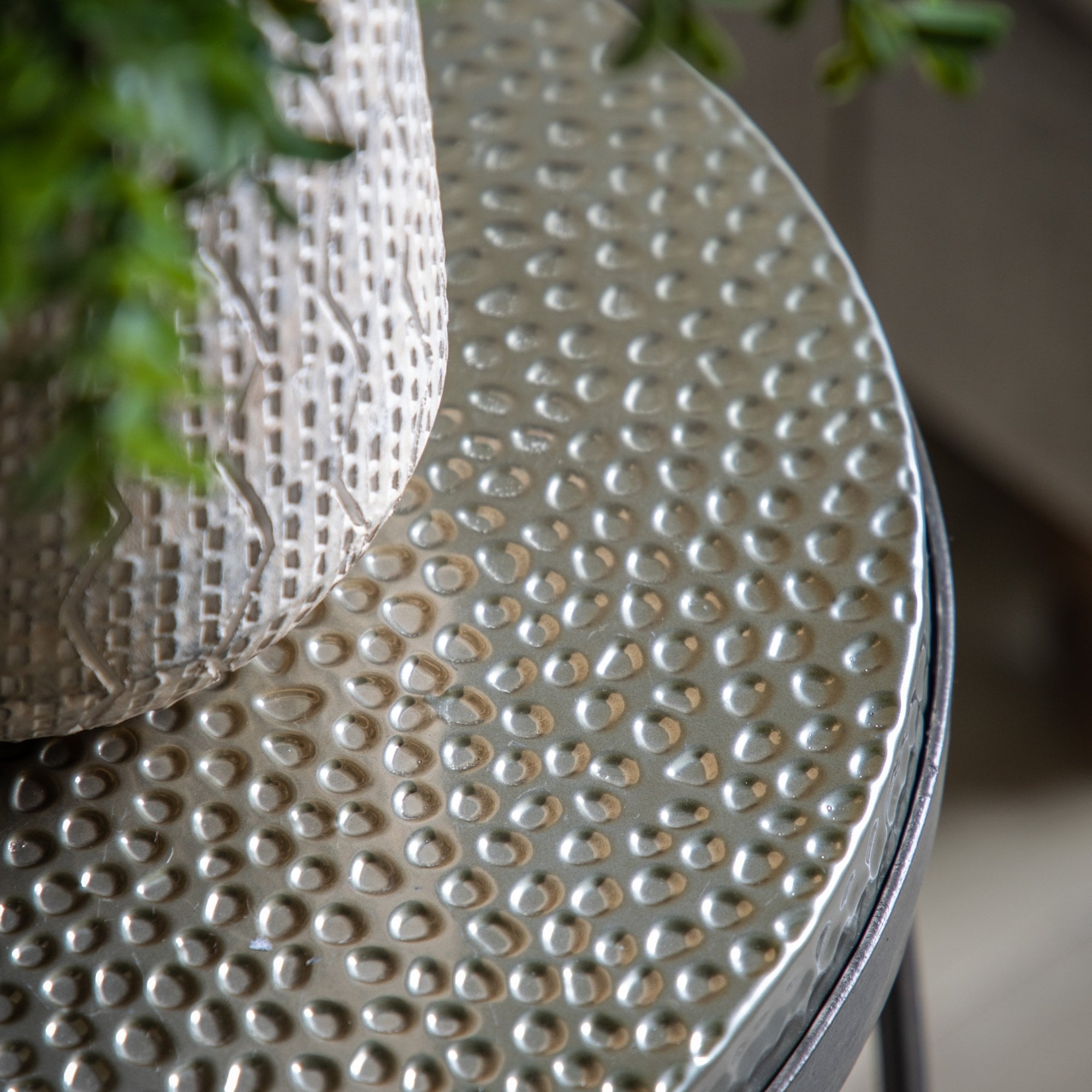 Close-up of the hammered metal top of a round side table with a plant on it.