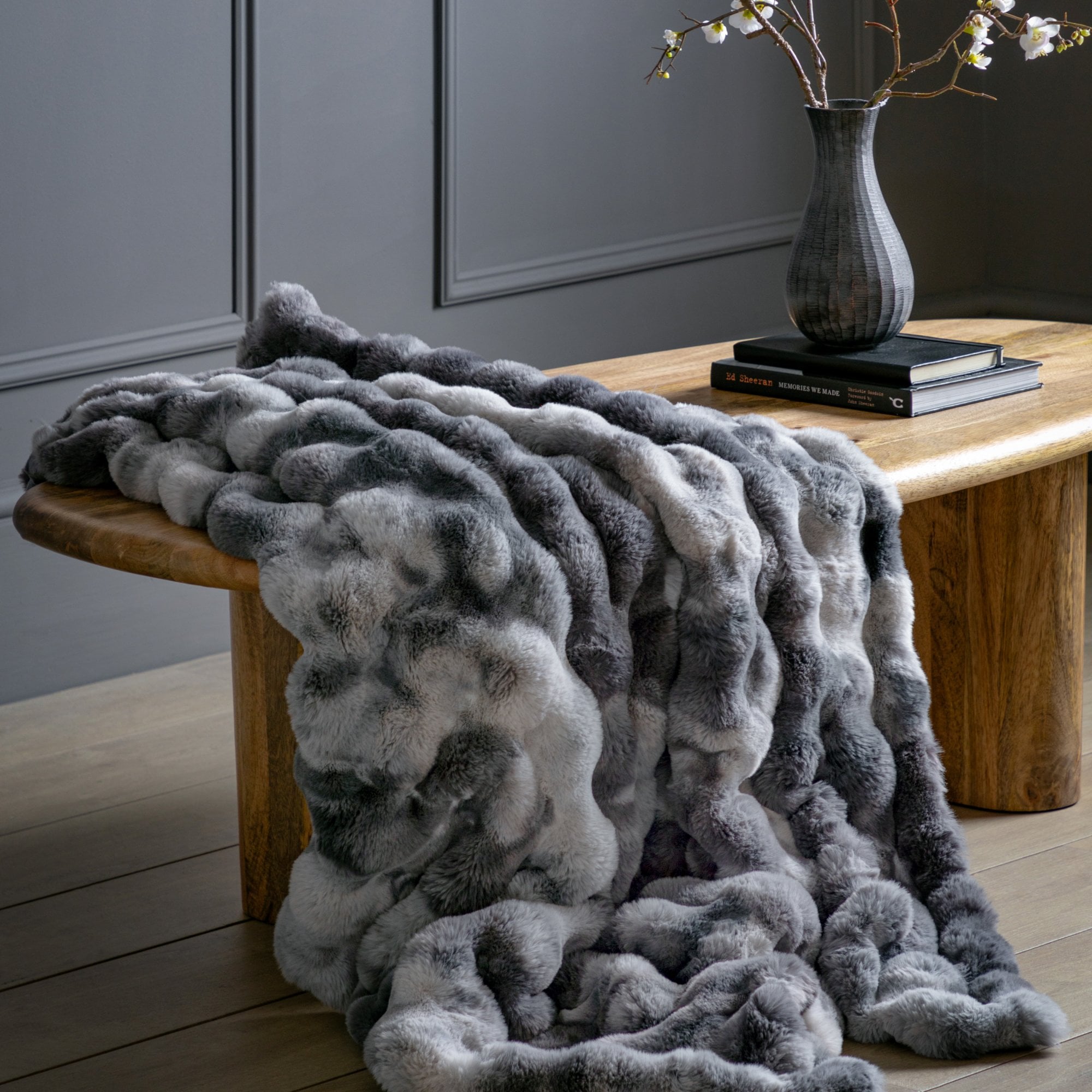 A luxurious gray and white faux fur throw blanket draped over a wooden bench.