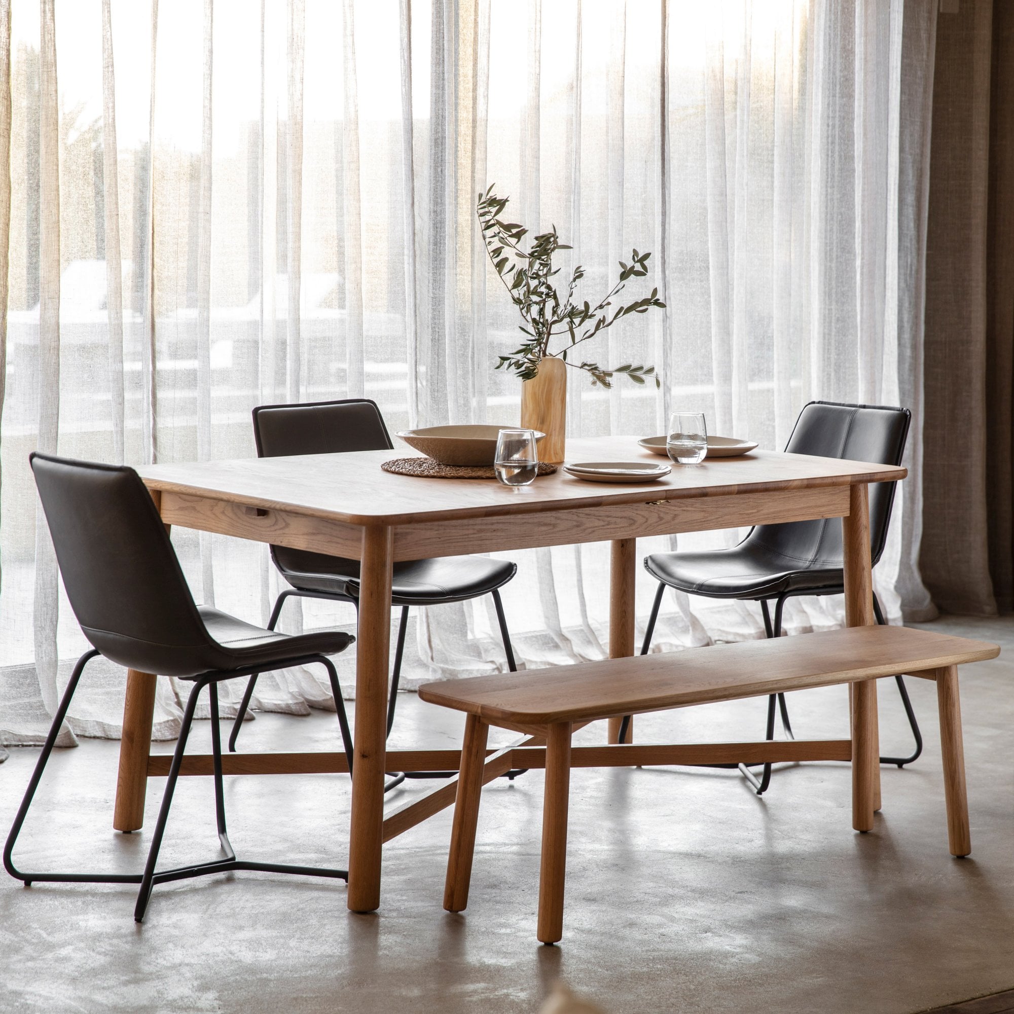 Light wood dining table set with black chairs and a matching bench.