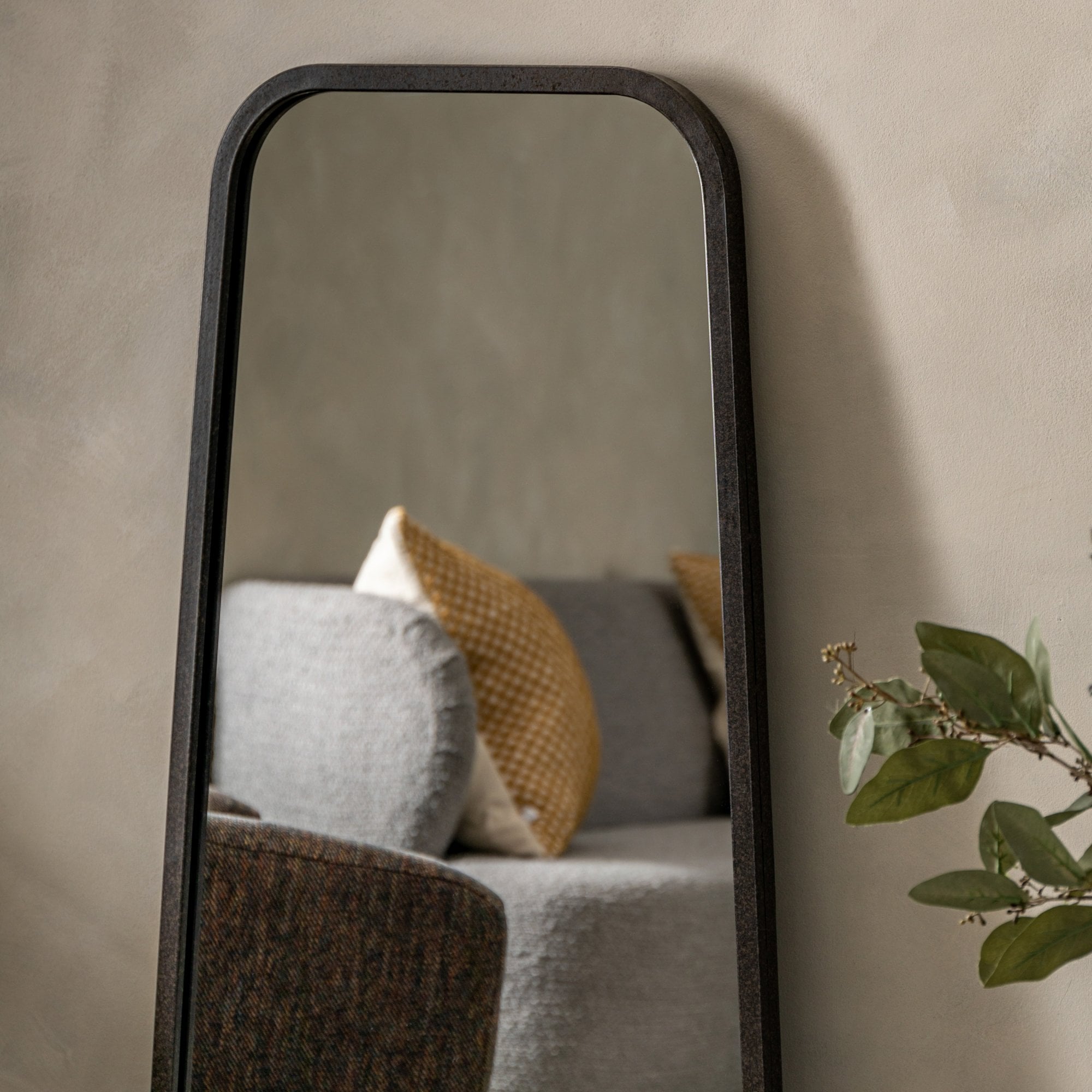 Close-up of the top portion of a dark-framed floor mirror reflecting a sofa.