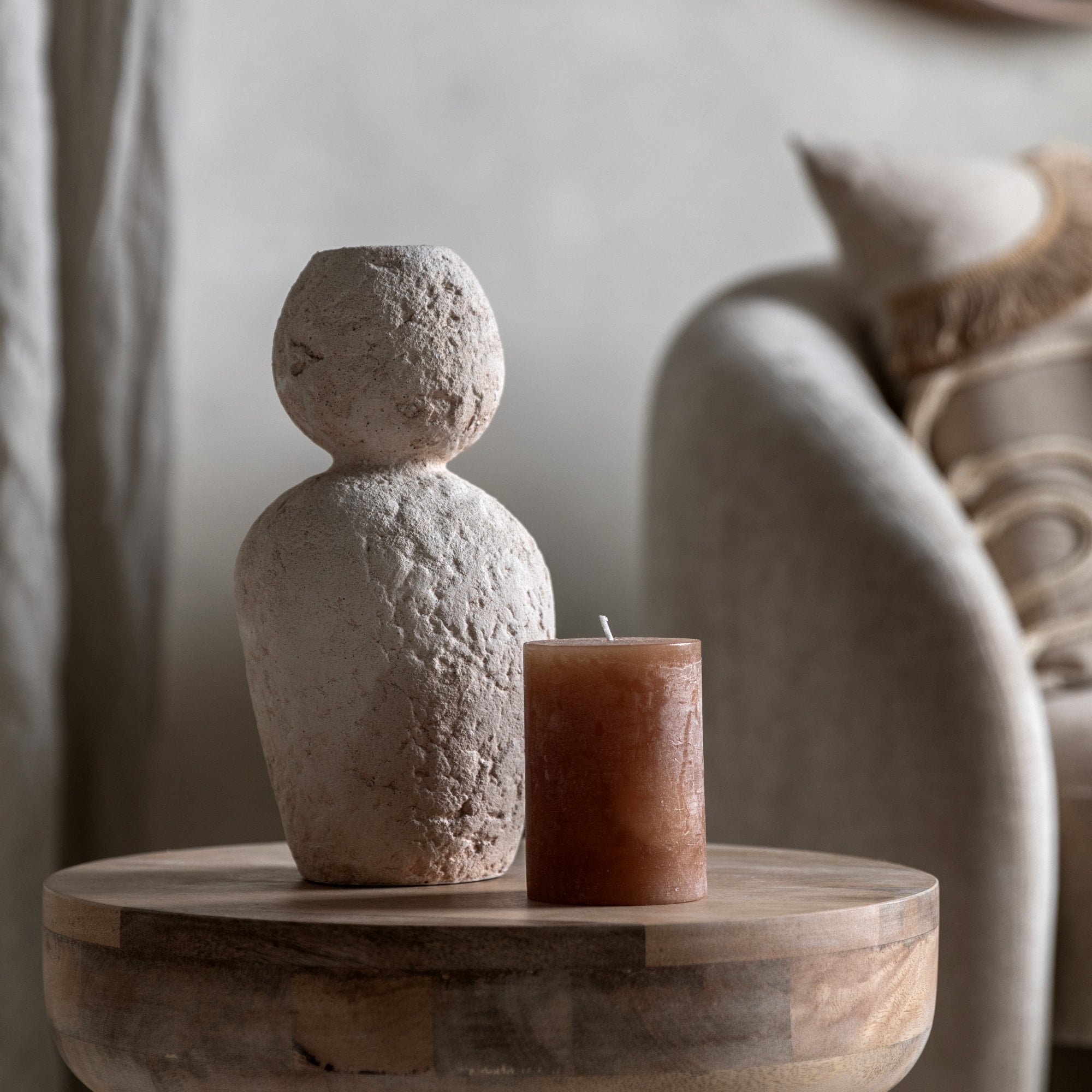 A white textured vase next to a brown candle on a wooden table.