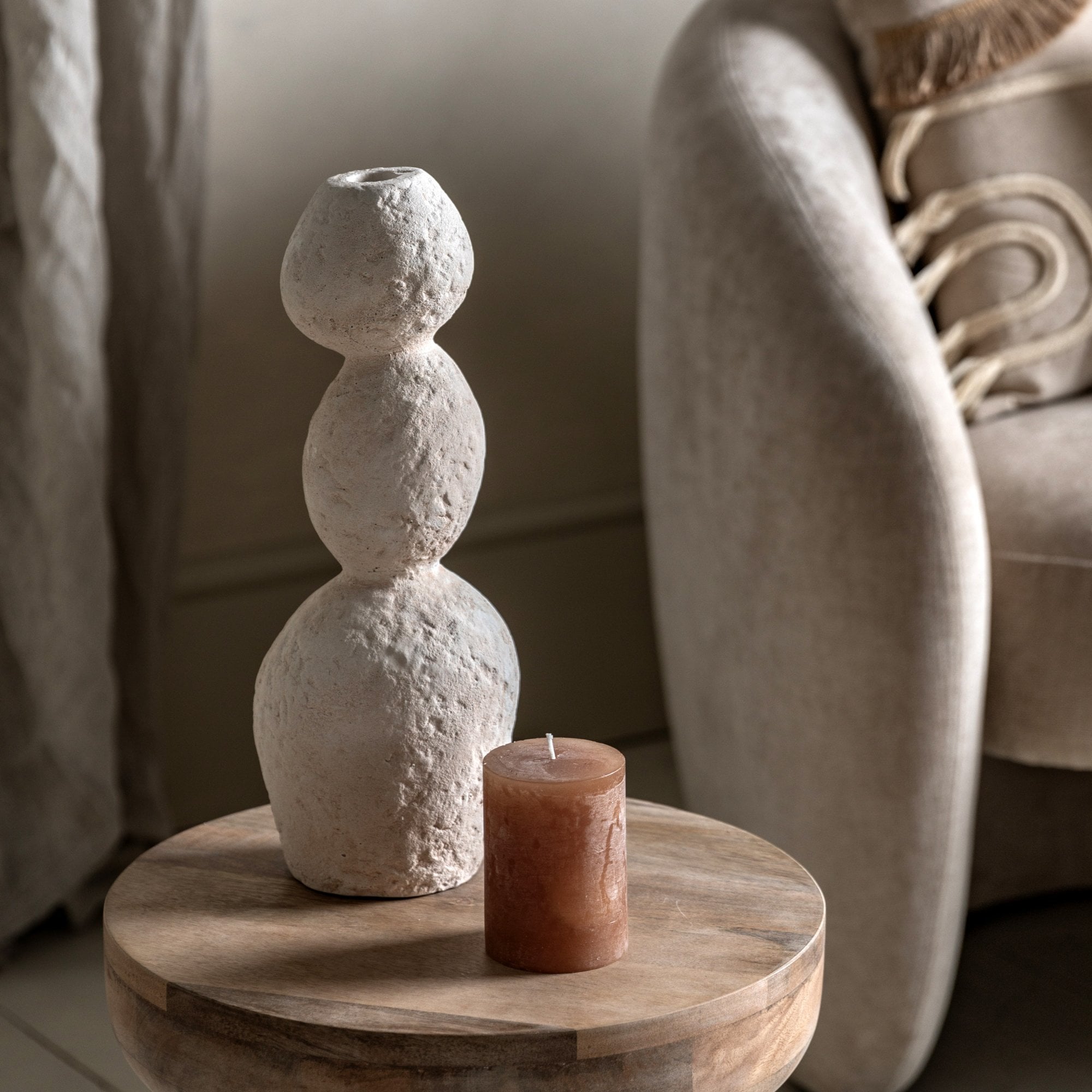 A textured white stacked stone vase with a brown candle on a wooden side table.