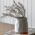 A white vase containing dried foliage sits on a newspaper, creating a rustic decor.