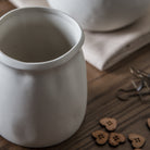 A white vase on a wooden surface with heart-shaped buttons and decorative items.