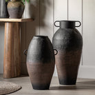 Two black and brown vases of different heights, next to a wooden console table.
