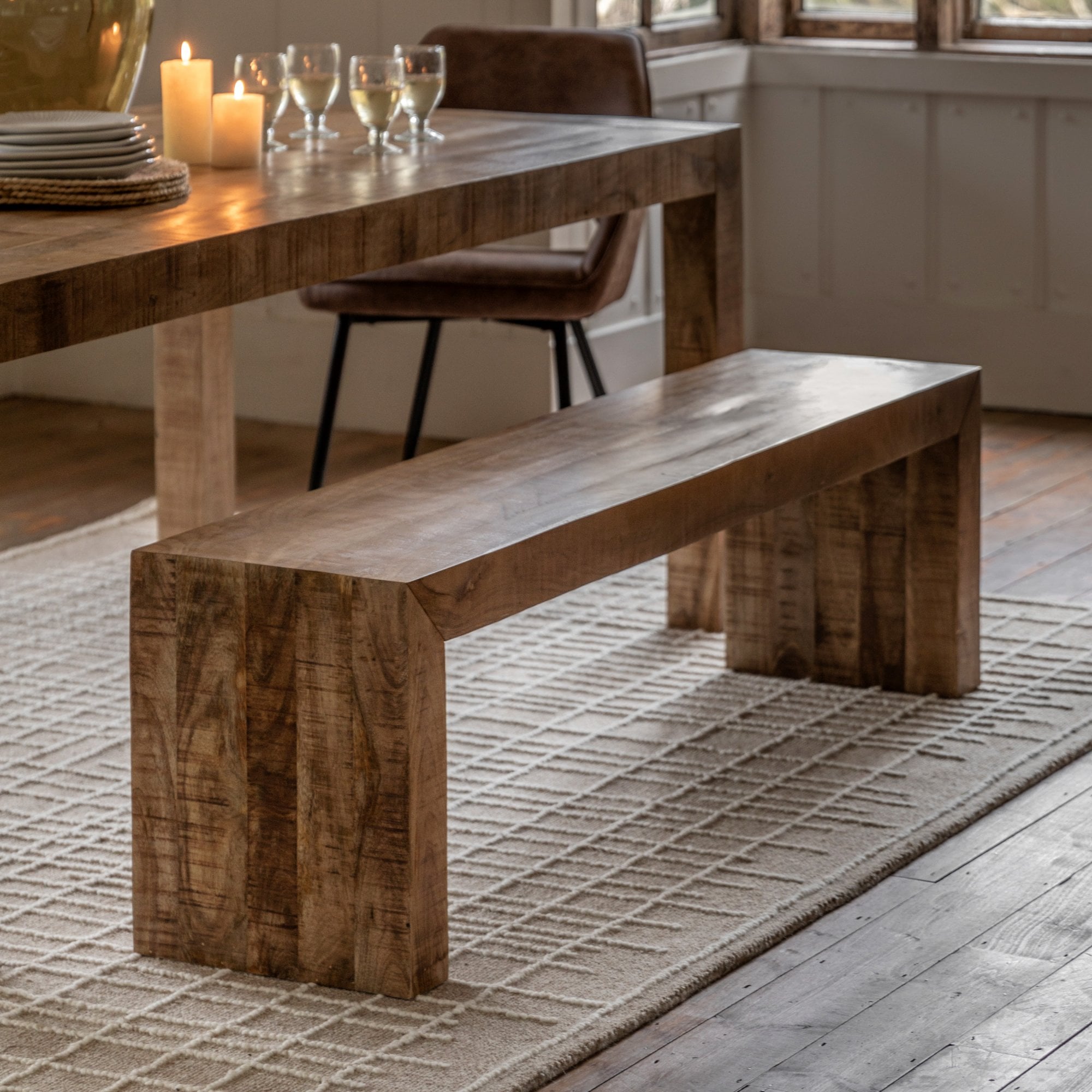 A rustic wooden bench positioned alongside a dining table set for a meal in a cozy room.