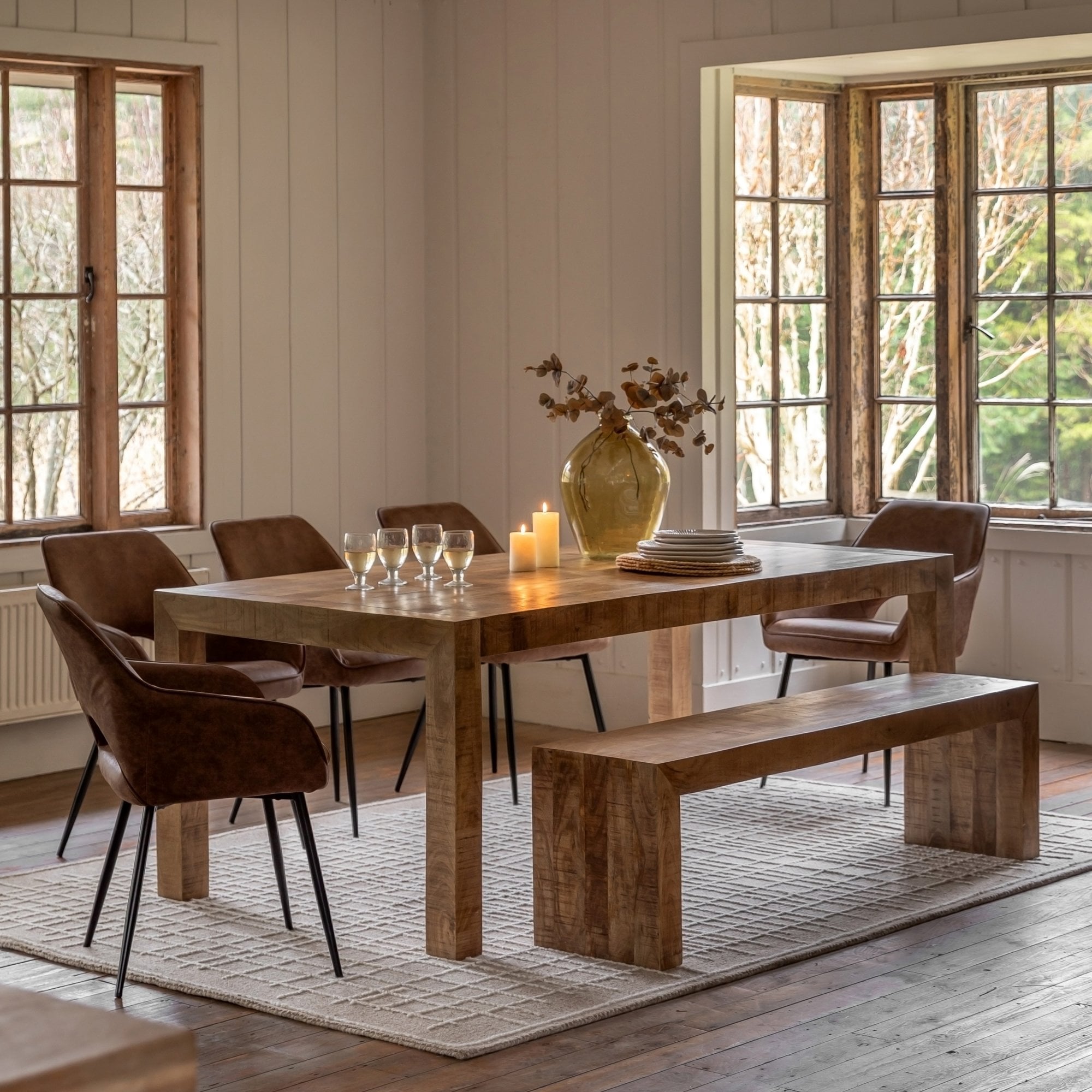 A rustic wooden dining table with chairs and a bench in a bright, airy room.