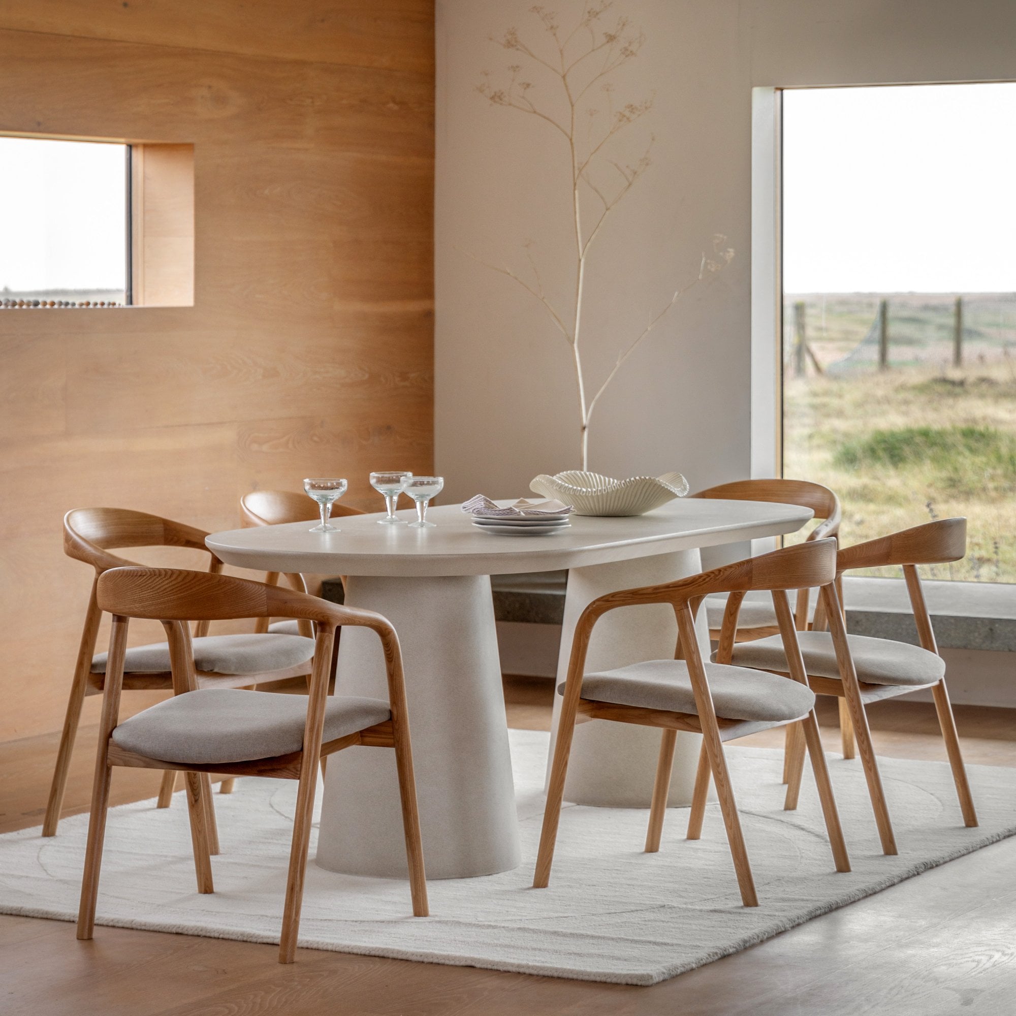 An oval dining table with pedestal bases, surrounded by wooden chairs in a modern dining room.