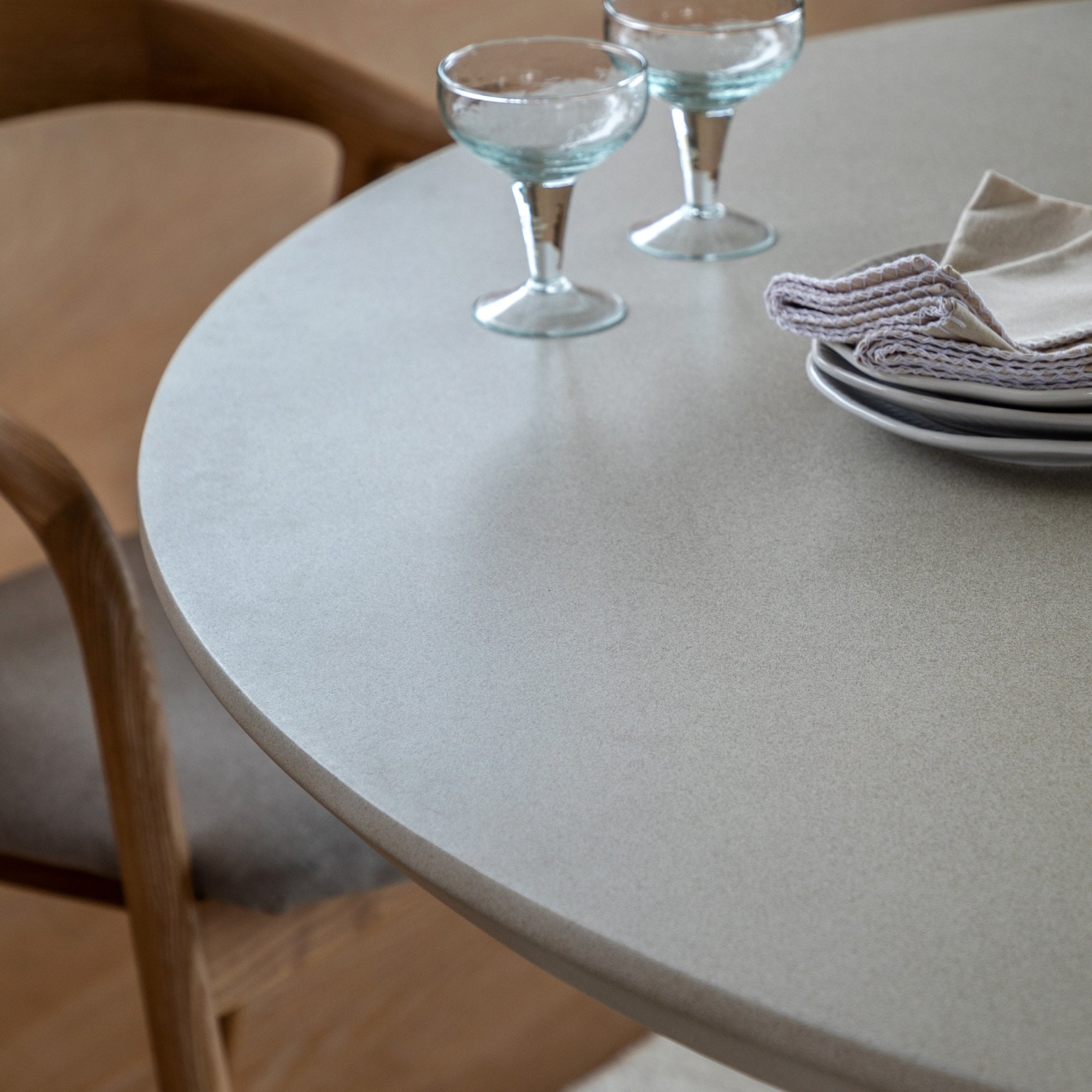 Close-up of a light grey round dining table with two glasses and stacked plates.