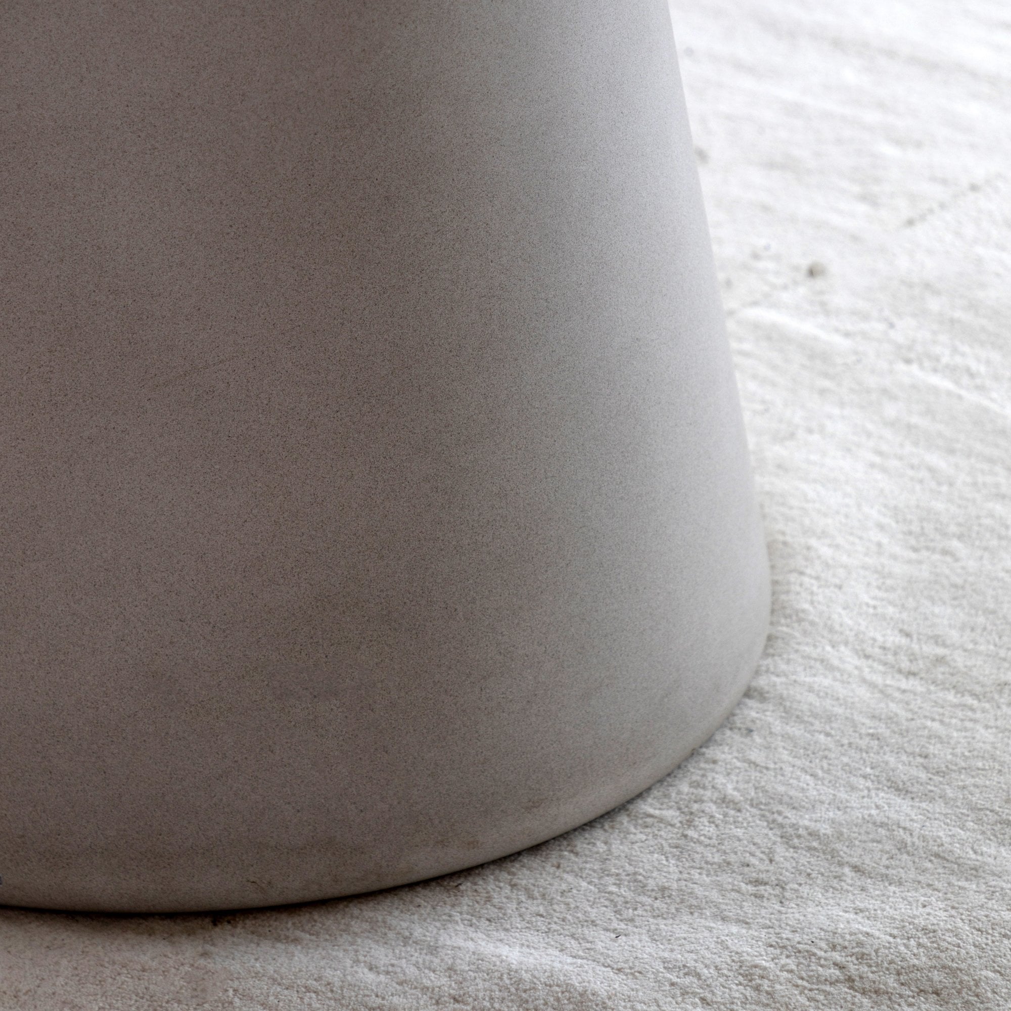 Close-up of the textured base of a light grey dining table on a white rug.
