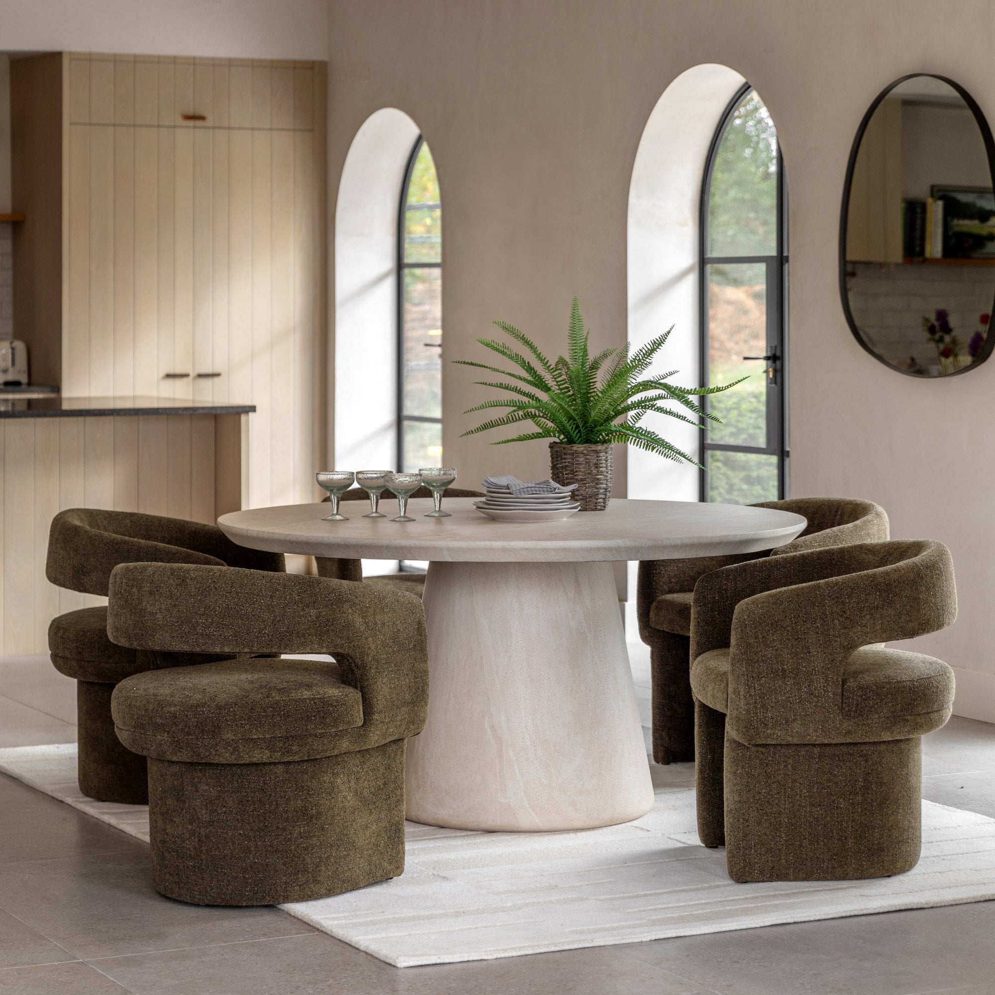 A modern dining room with a round travertine table and four olive green swivel chairs.