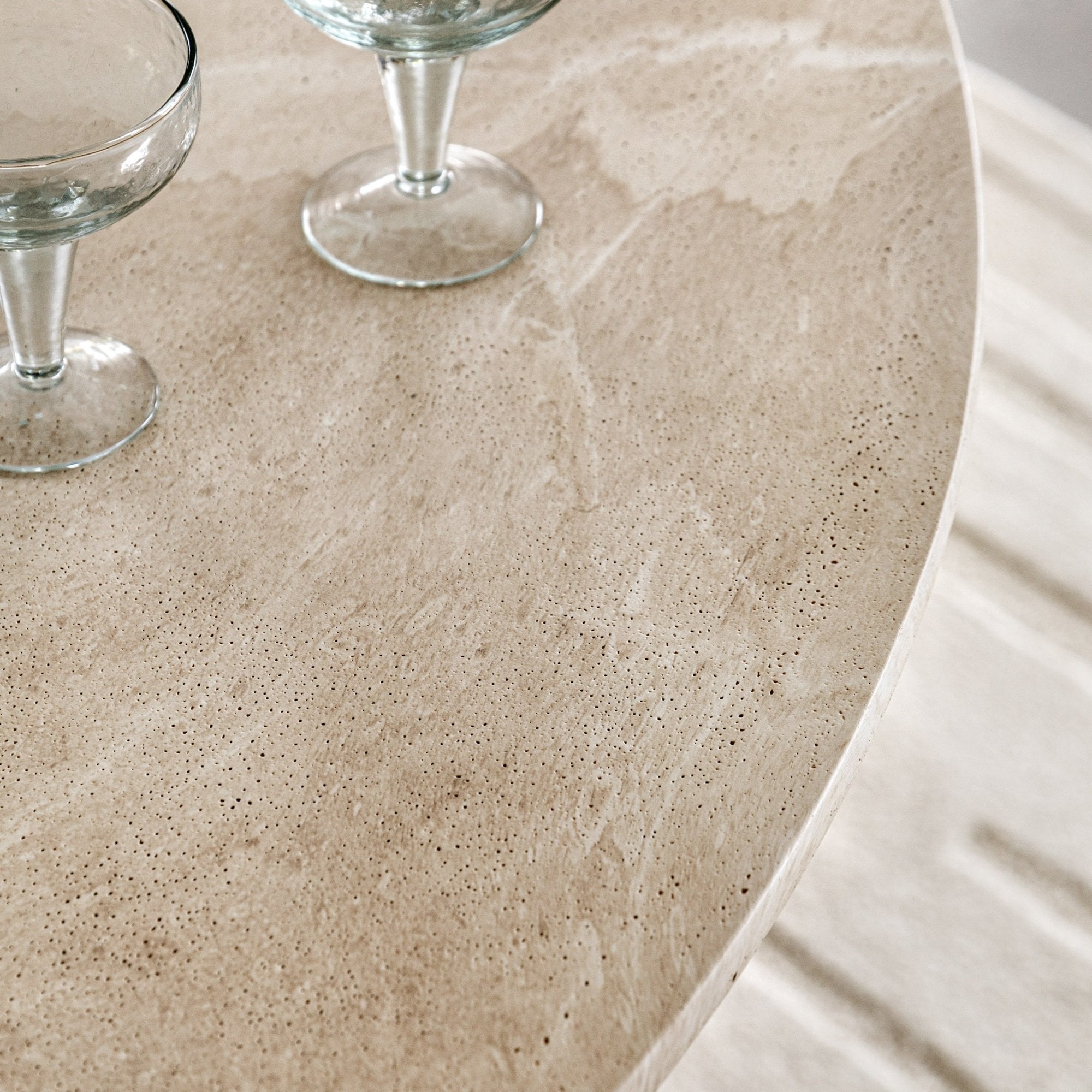 Close-up of the textured travertine tabletop with two empty martini glasses.