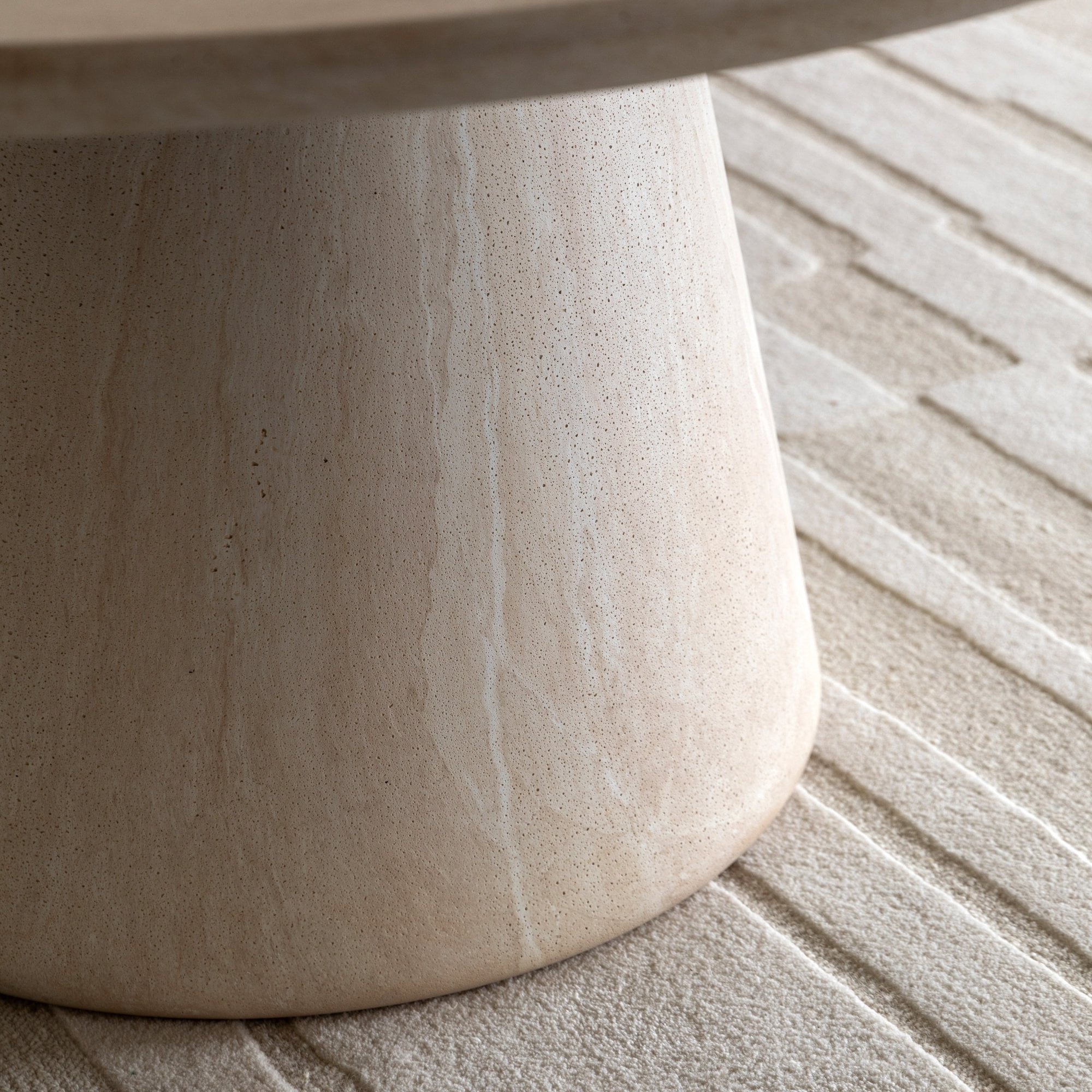 Close-up of the conical travertine pedestal base of a dining table on a light rug.