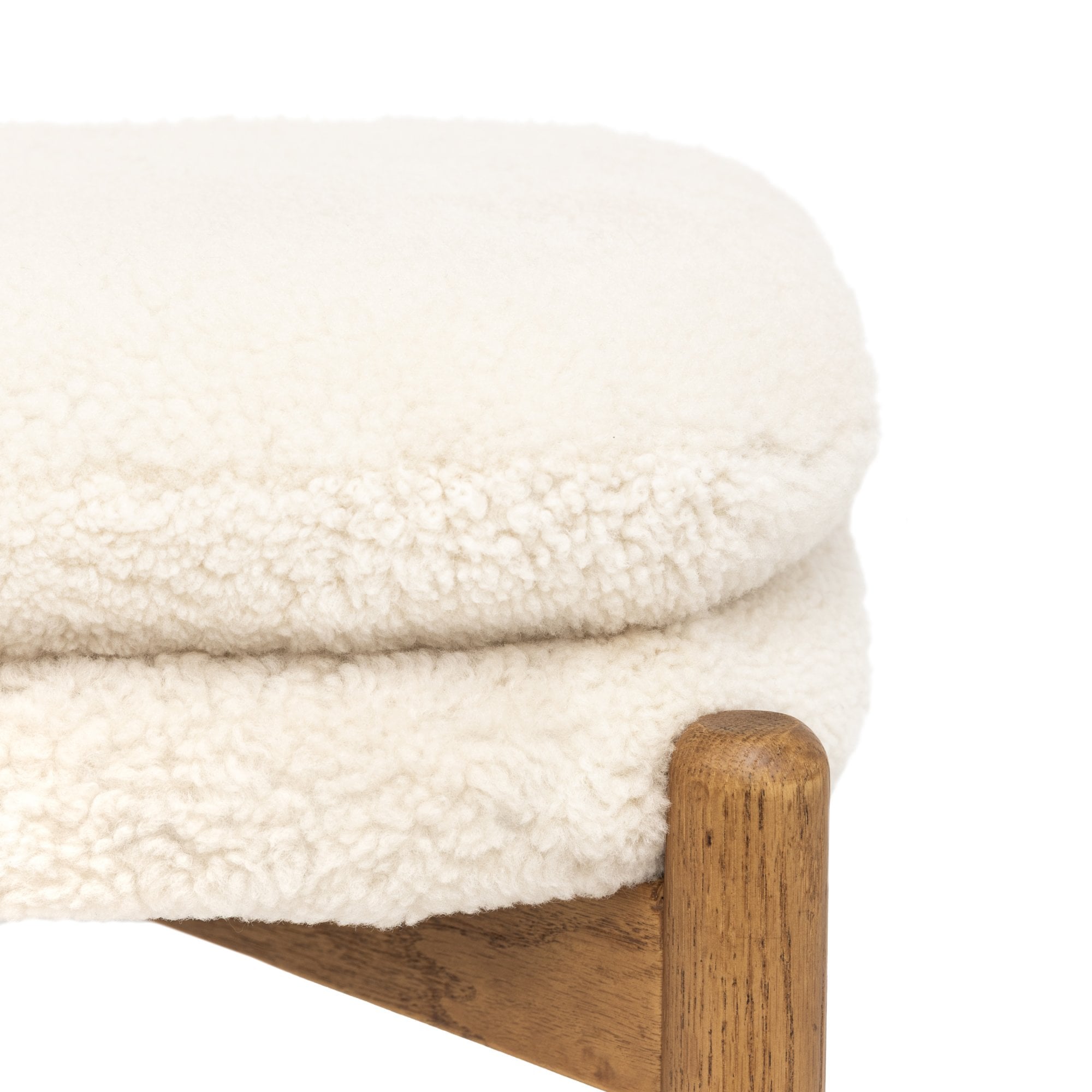 Close-up of the white sheepskin upholstery and wooden frame of a footstool on white.