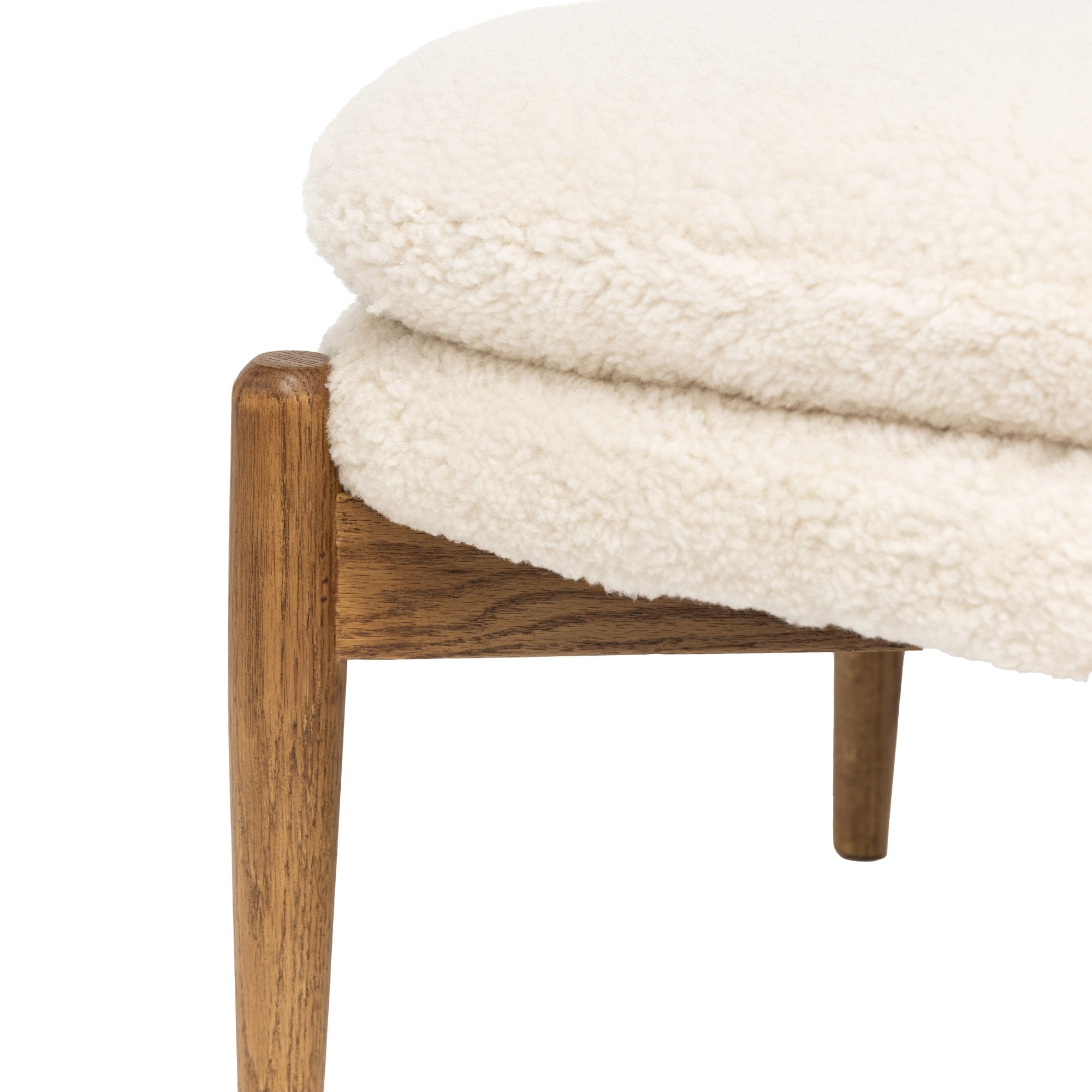 Close-up of the white sheepskin upholstery and wooden frame of a footstool on white.