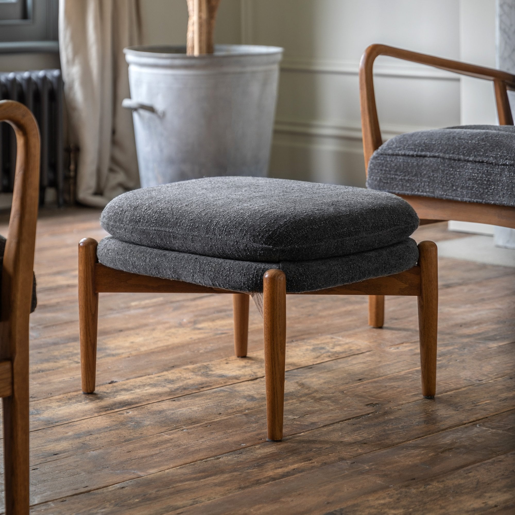A mid-century modern ottoman in a living room setting, featuring a grey upholstered cushion.
