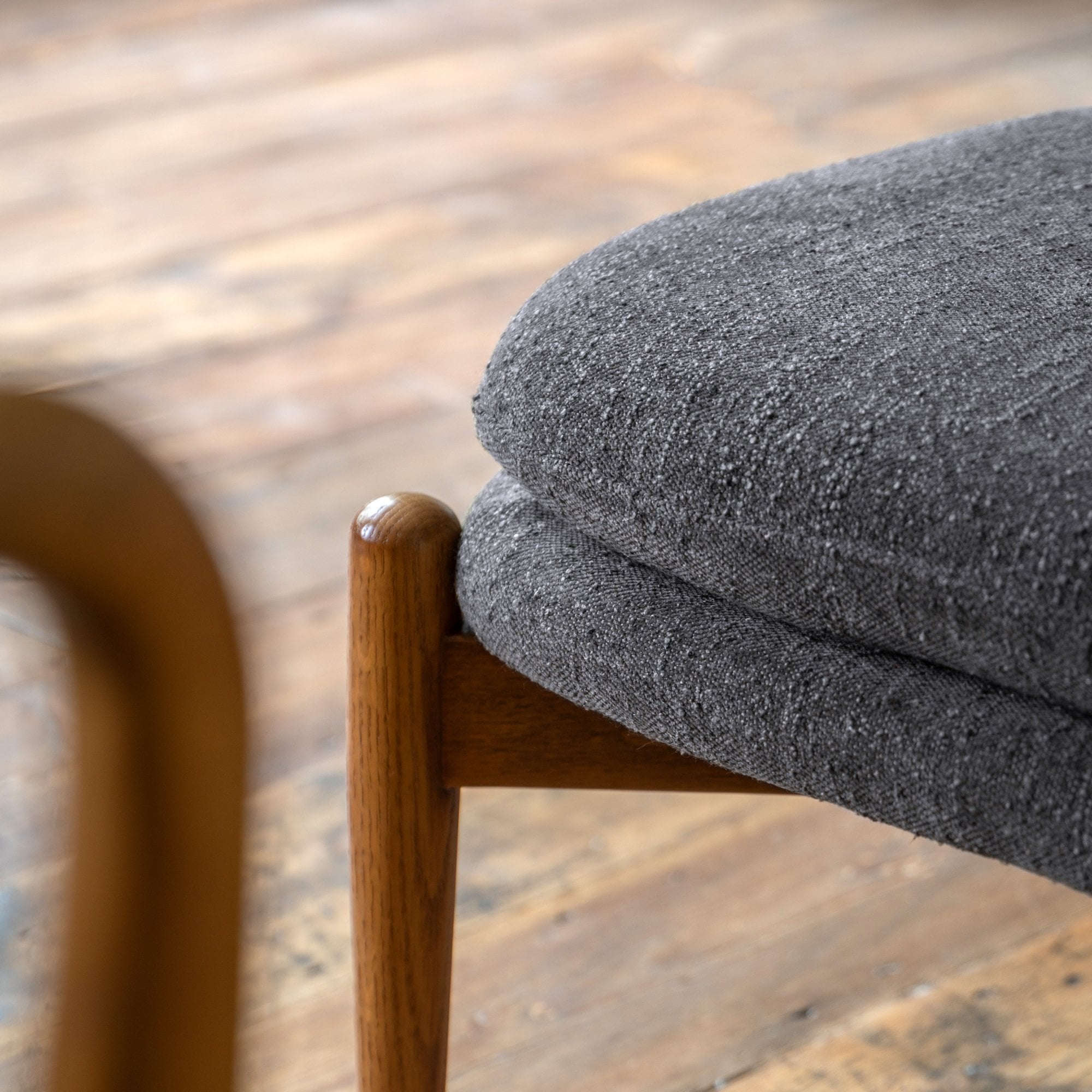 Close-up of the grey textured fabric cushion and rounded wooden leg of an ottoman.