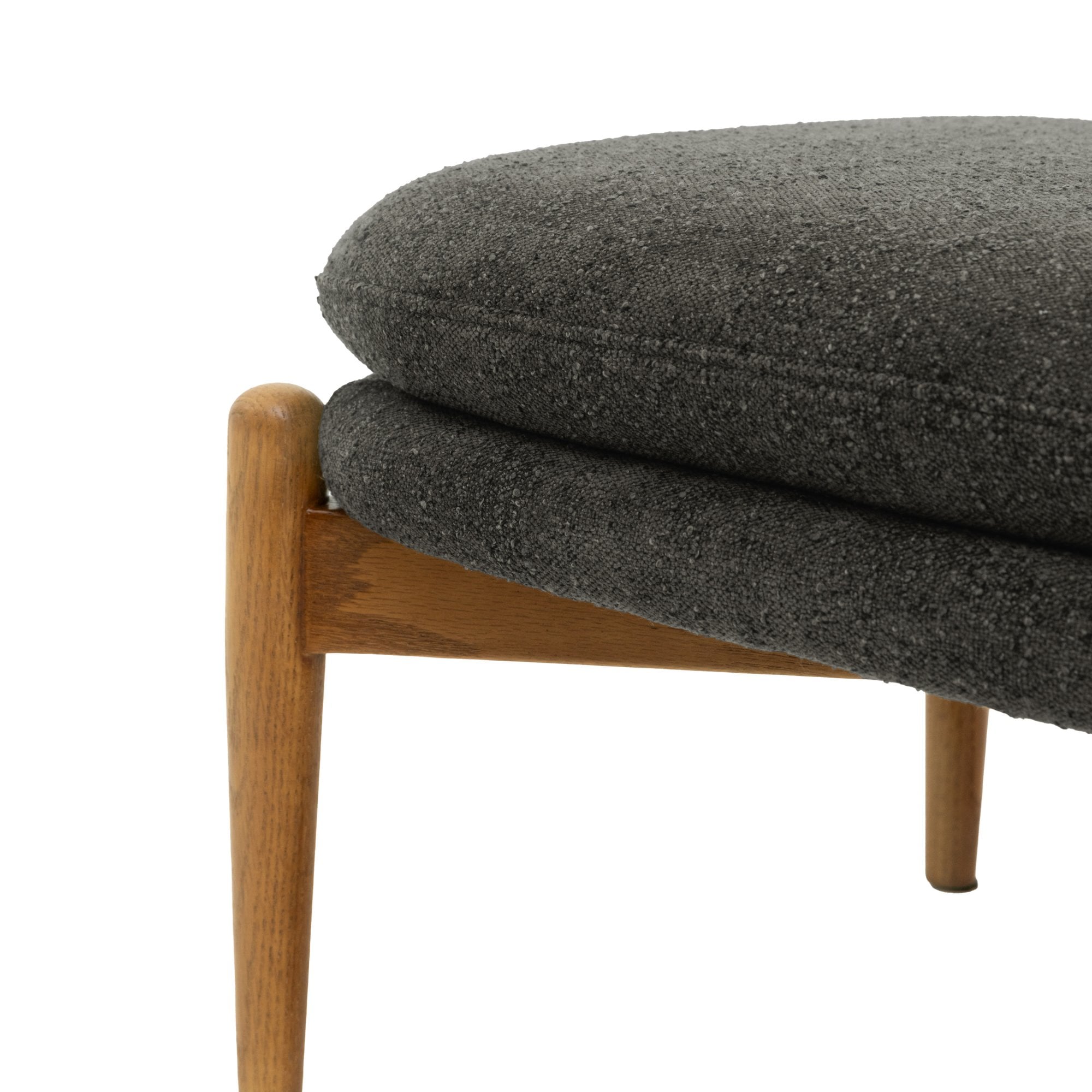 Side view of a mid-century modern ottoman, showing grey cushions and a wooden leg.