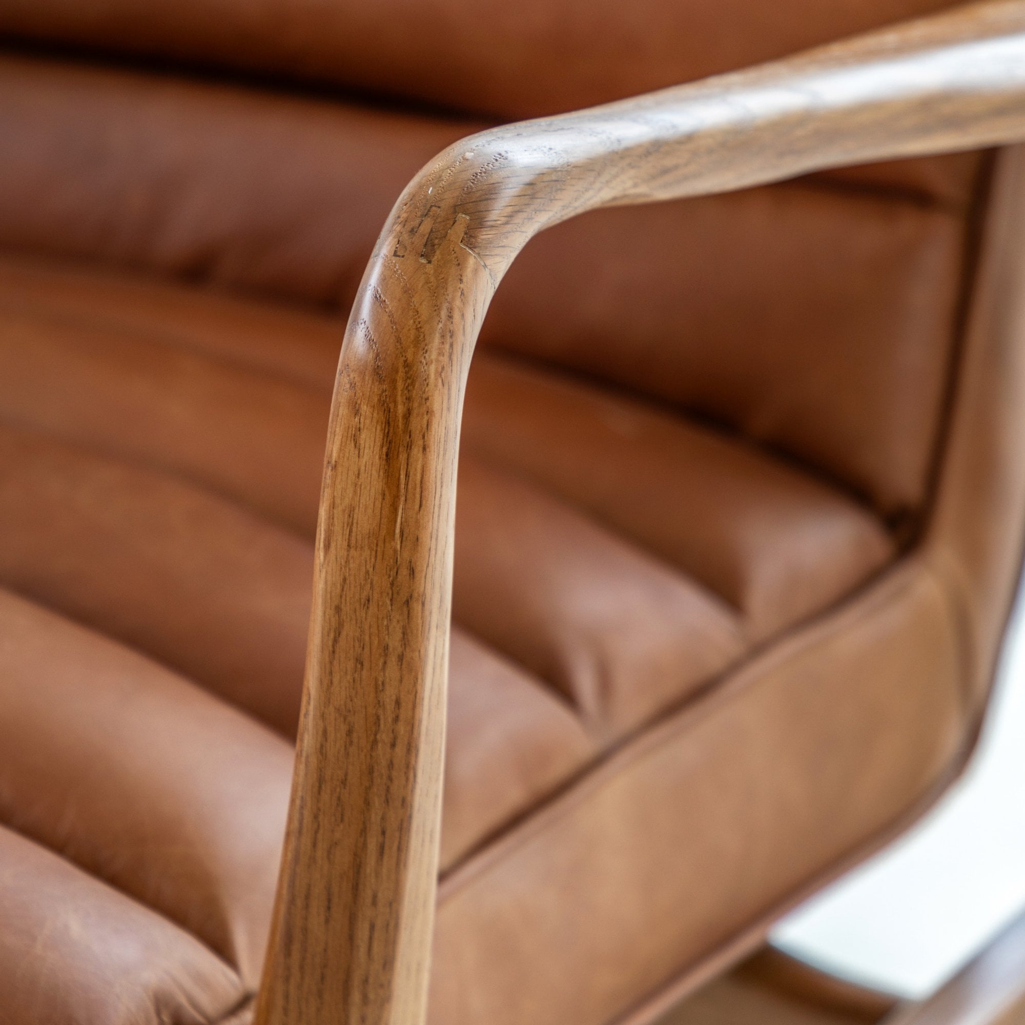 Close-up of the curved wooden armrest of a brown leather armchair.