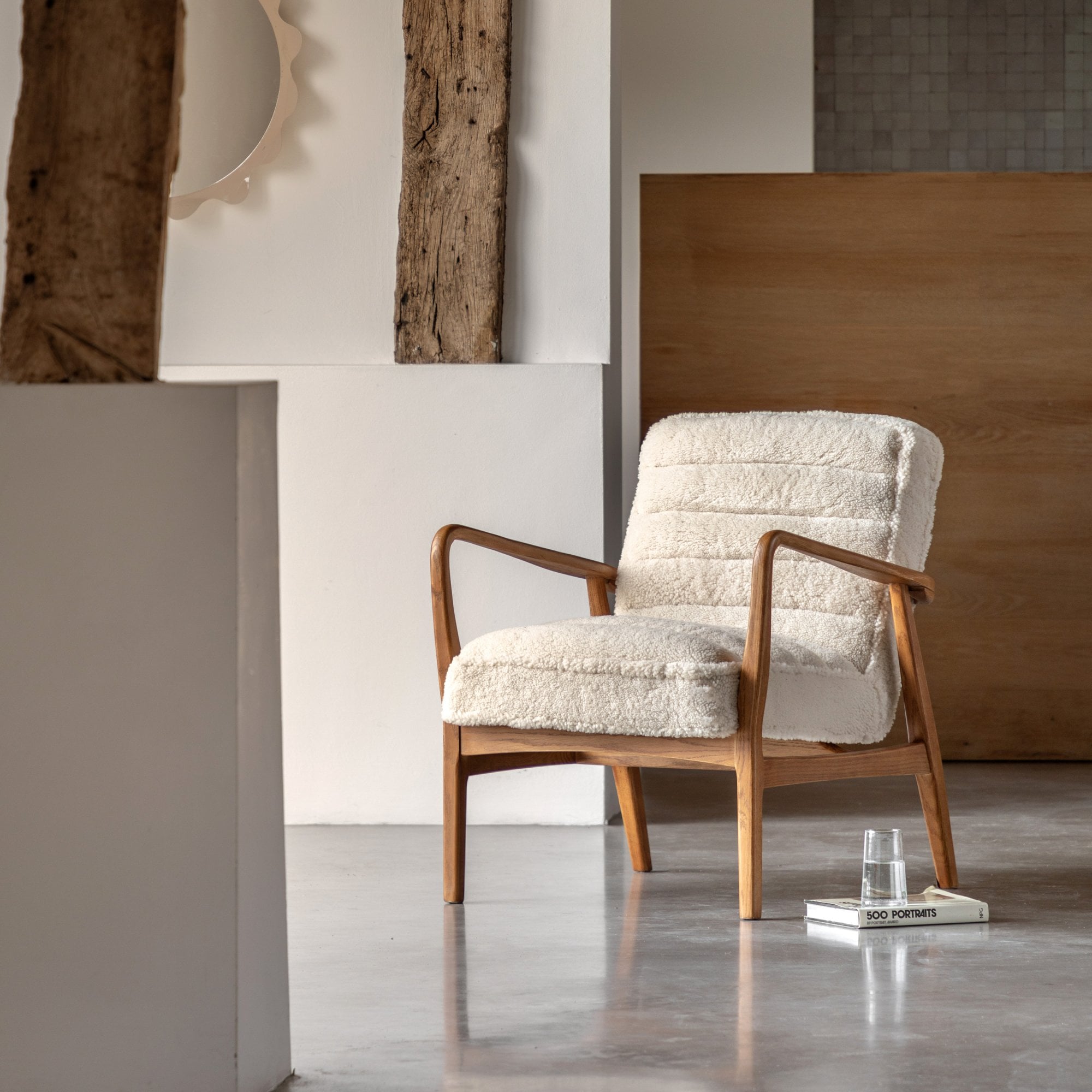 Cream-colored armchair with wood frame in a bright room with a rustic column.