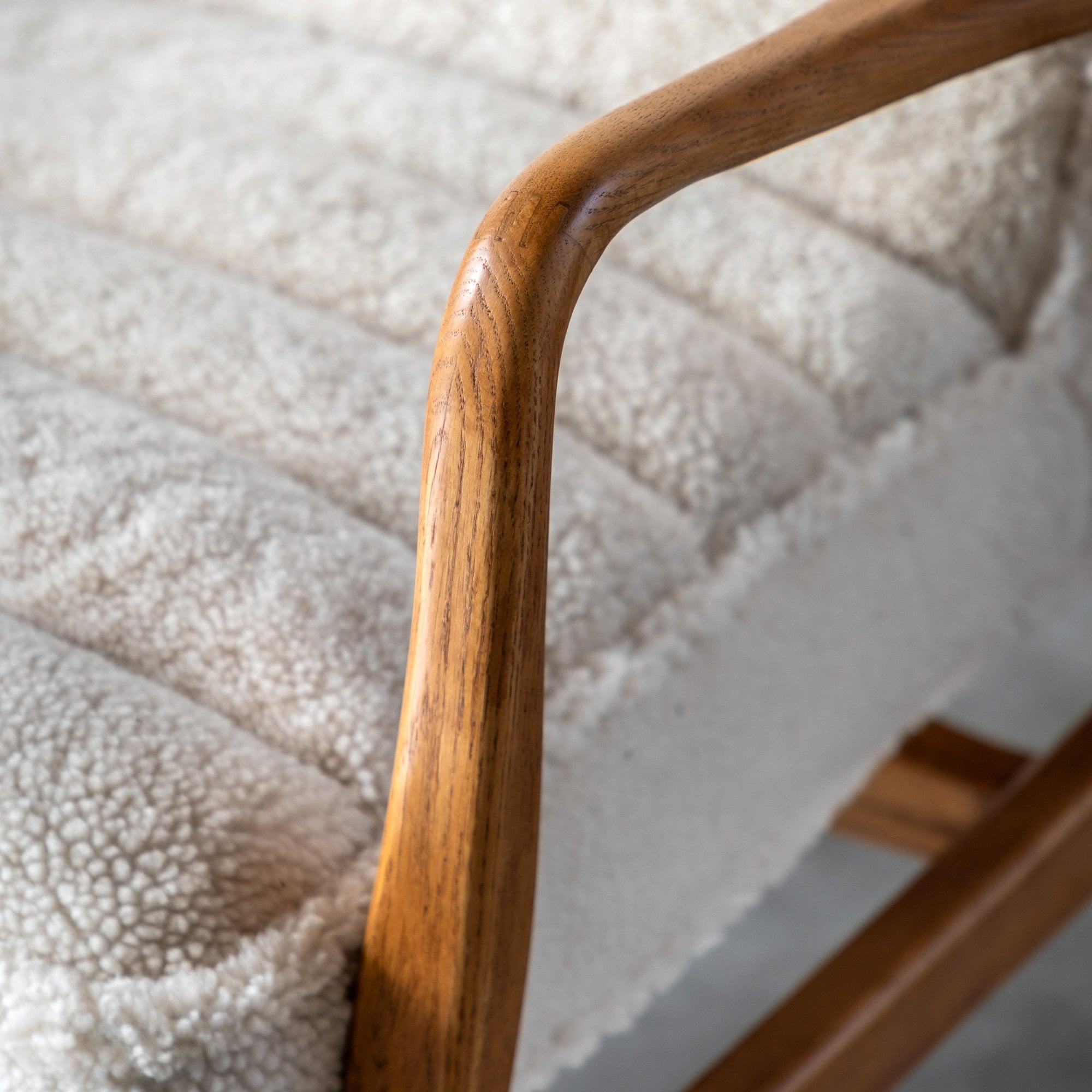 Close-up of the smooth wood armrest and fluffy cream-colored upholstery of an armchair.