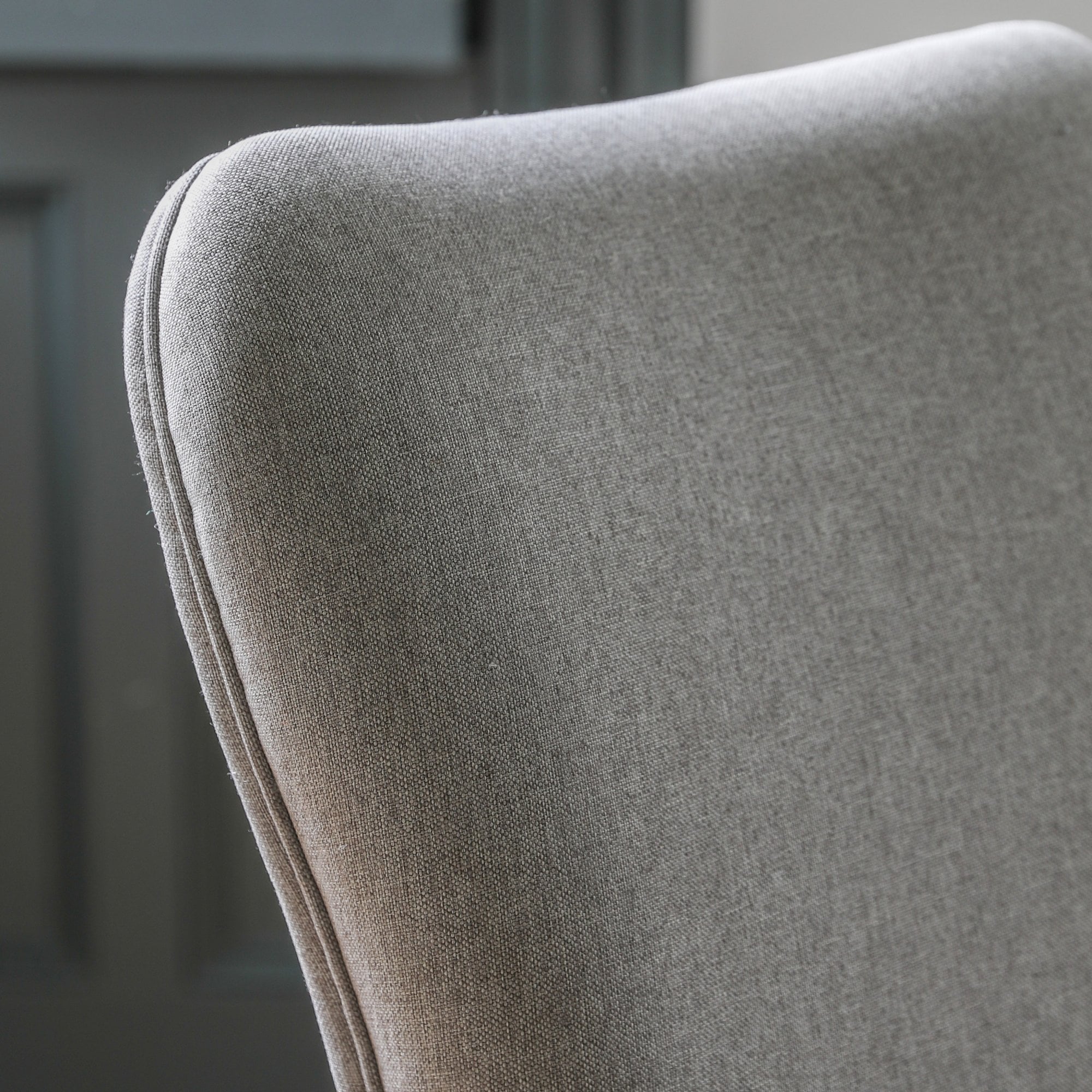 Close-up of the curved top of the grey fabric upholstered dining chair's backrest.