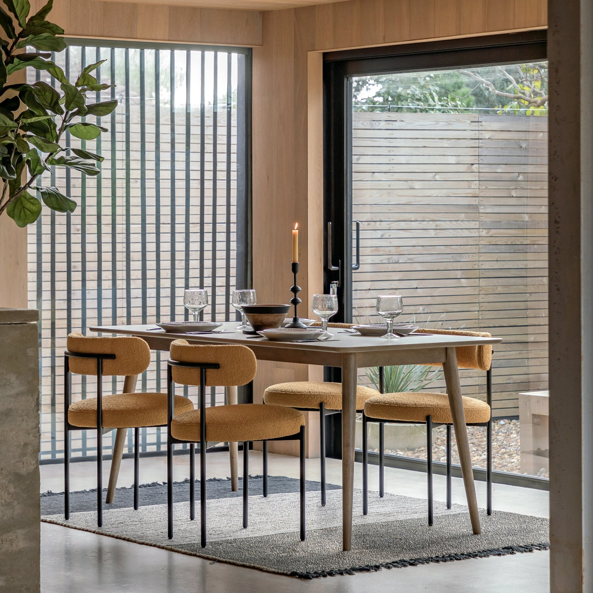 A modern dining room with a long wooden table and four mustard yellow chairs.