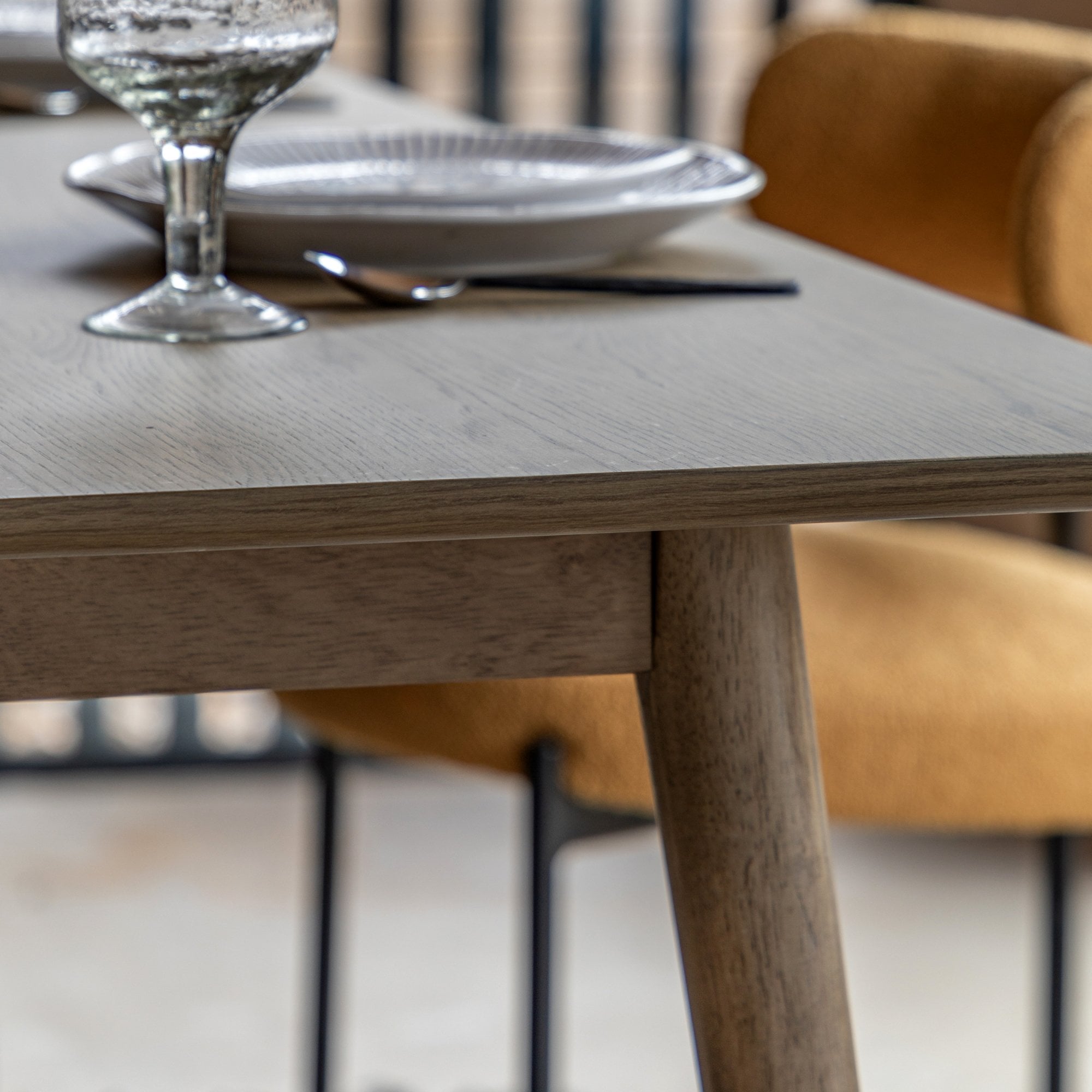 Close-up of the light wood grain on the dining table, set with a glass and plate.
