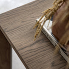 Close-up of the wooden tabletop, showing a vase with dried grass and a book.