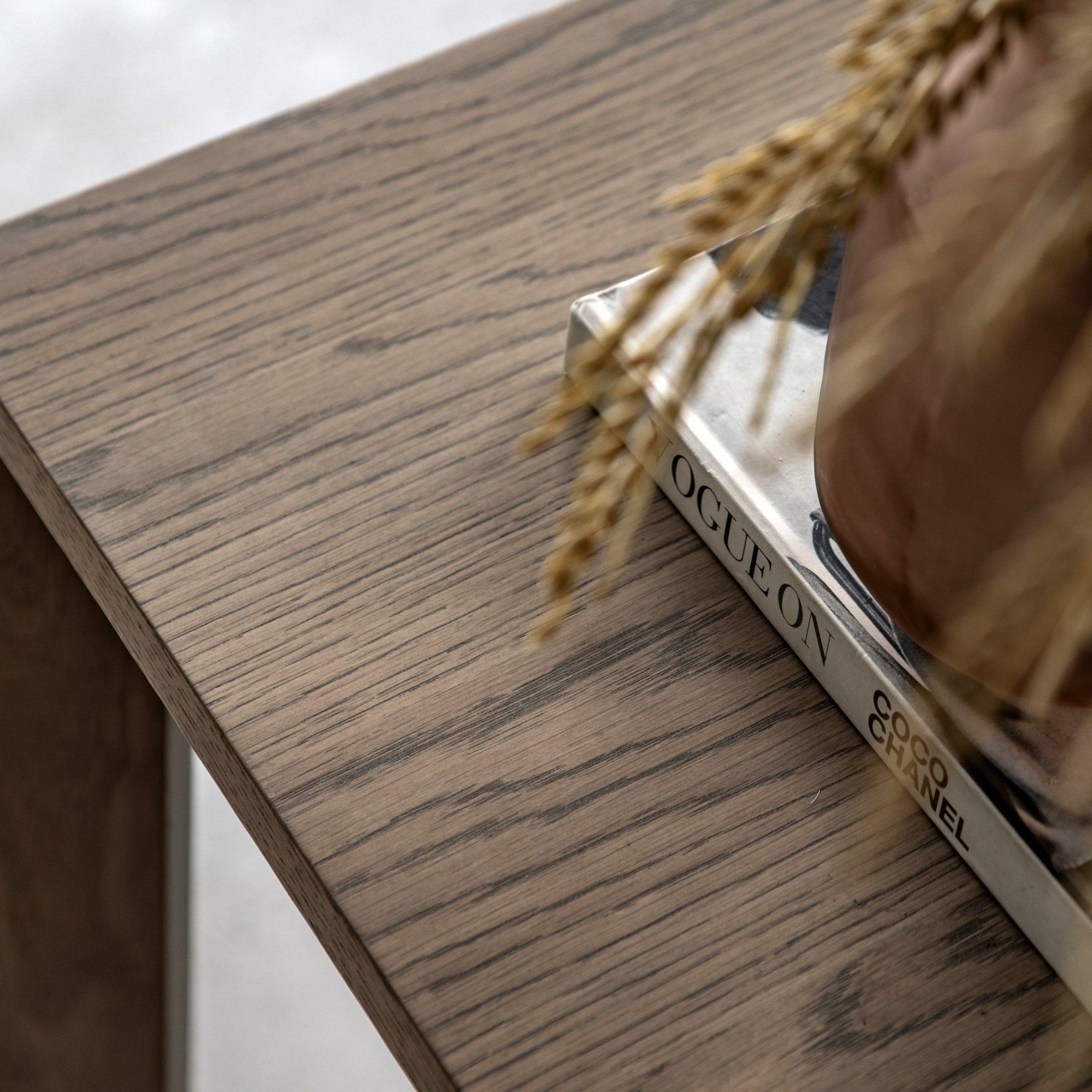 Close-up of the wooden tabletop, showing a vase with dried grass and a book.