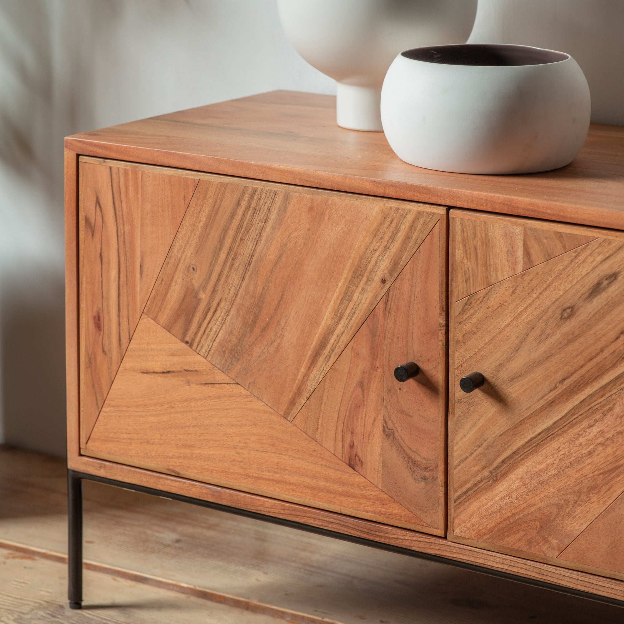 Close-up of a natural wood cabinet with geometric patterned doors and black handles.