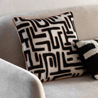 A black and white patterned throw pillow with an orange border rests on a light-colored sofa.