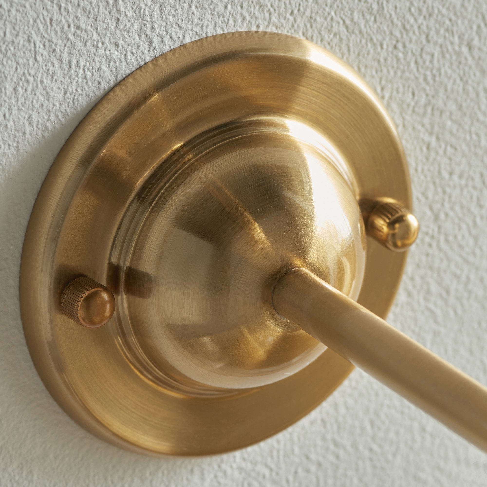 Close-up of the brass base of a wall light fixture, showing mounting details.