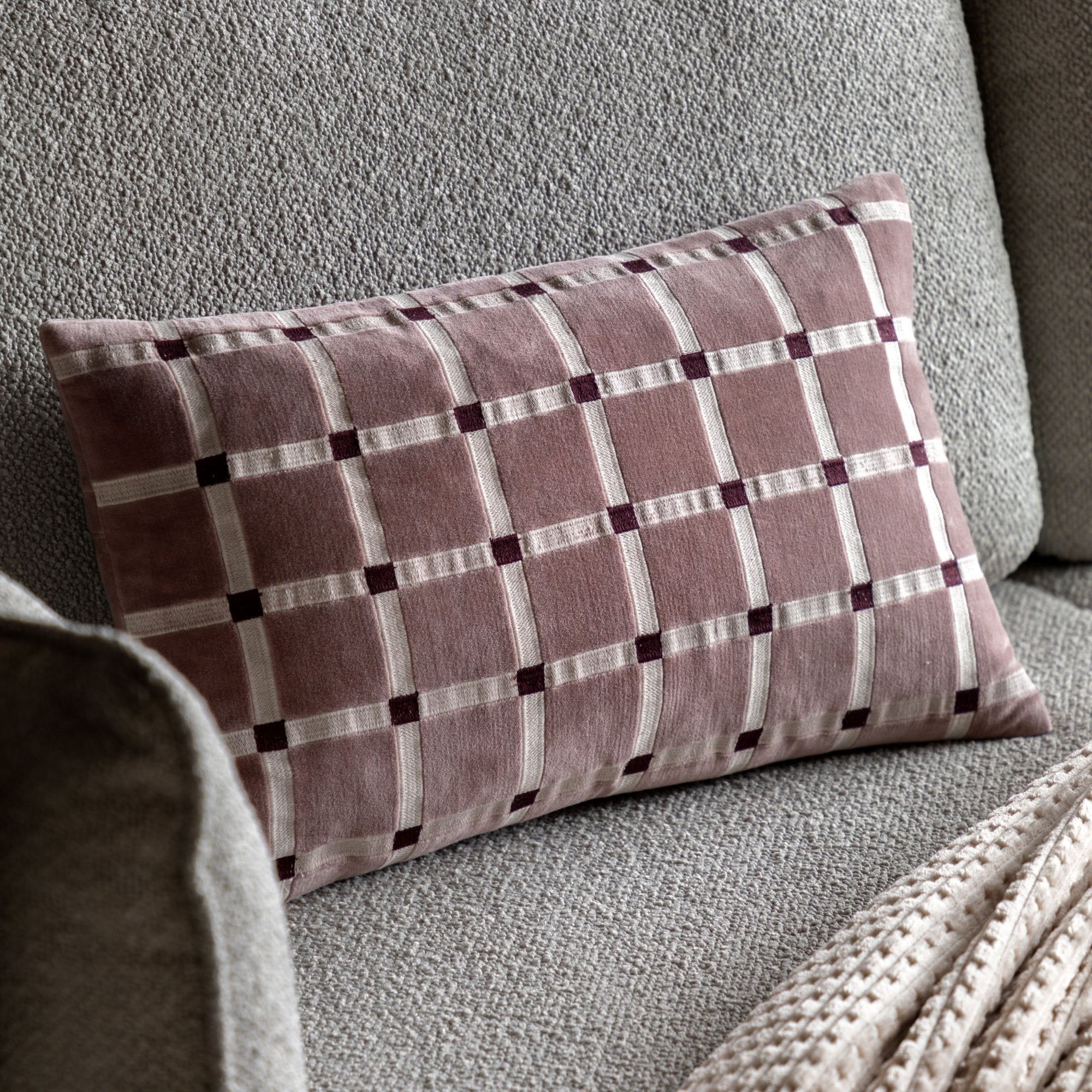 Pink lumbar pillow with checkerboard pattern on a gray sofa.