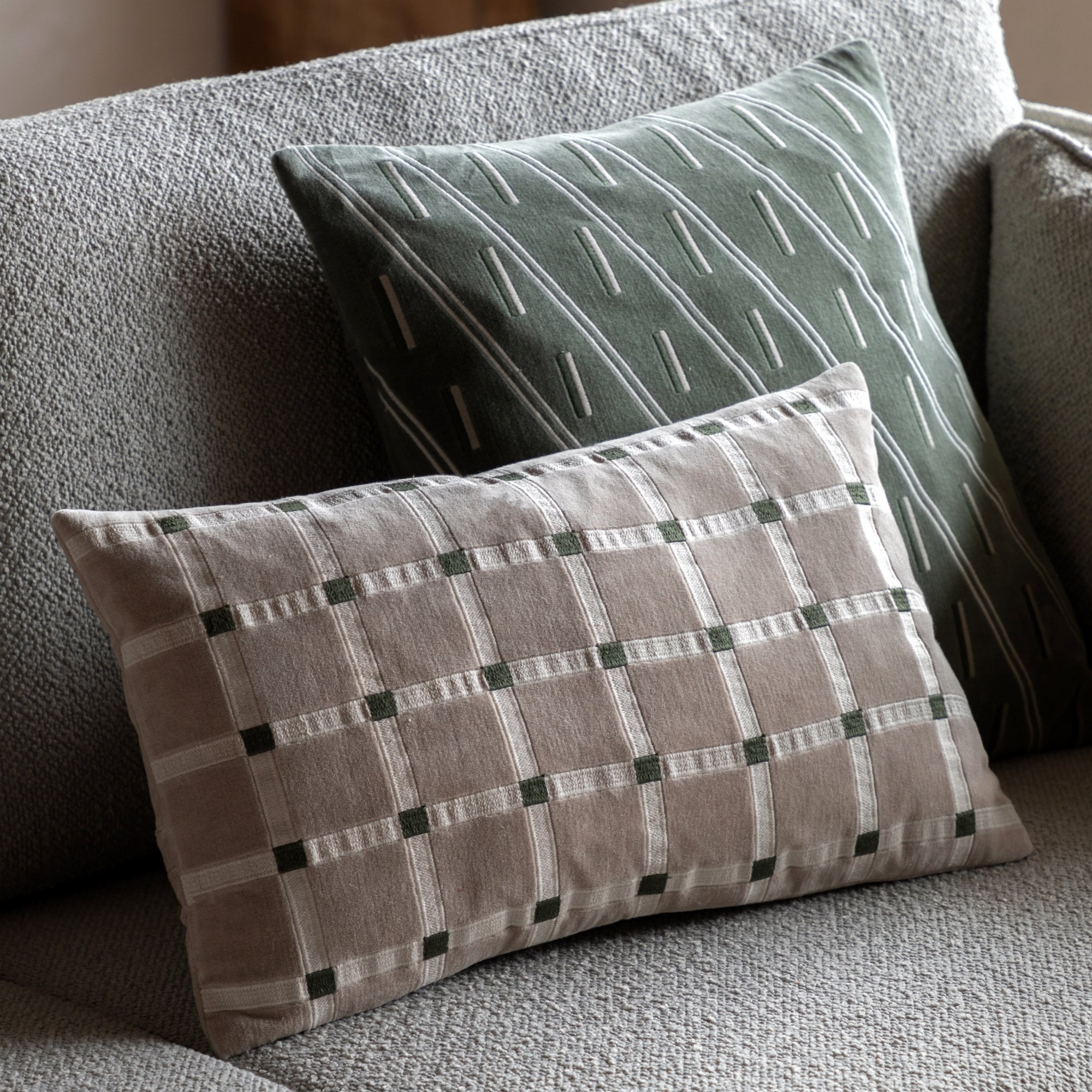 A beige and white plaid throw pillow rests on a gray sofa next to a green striped pillow.