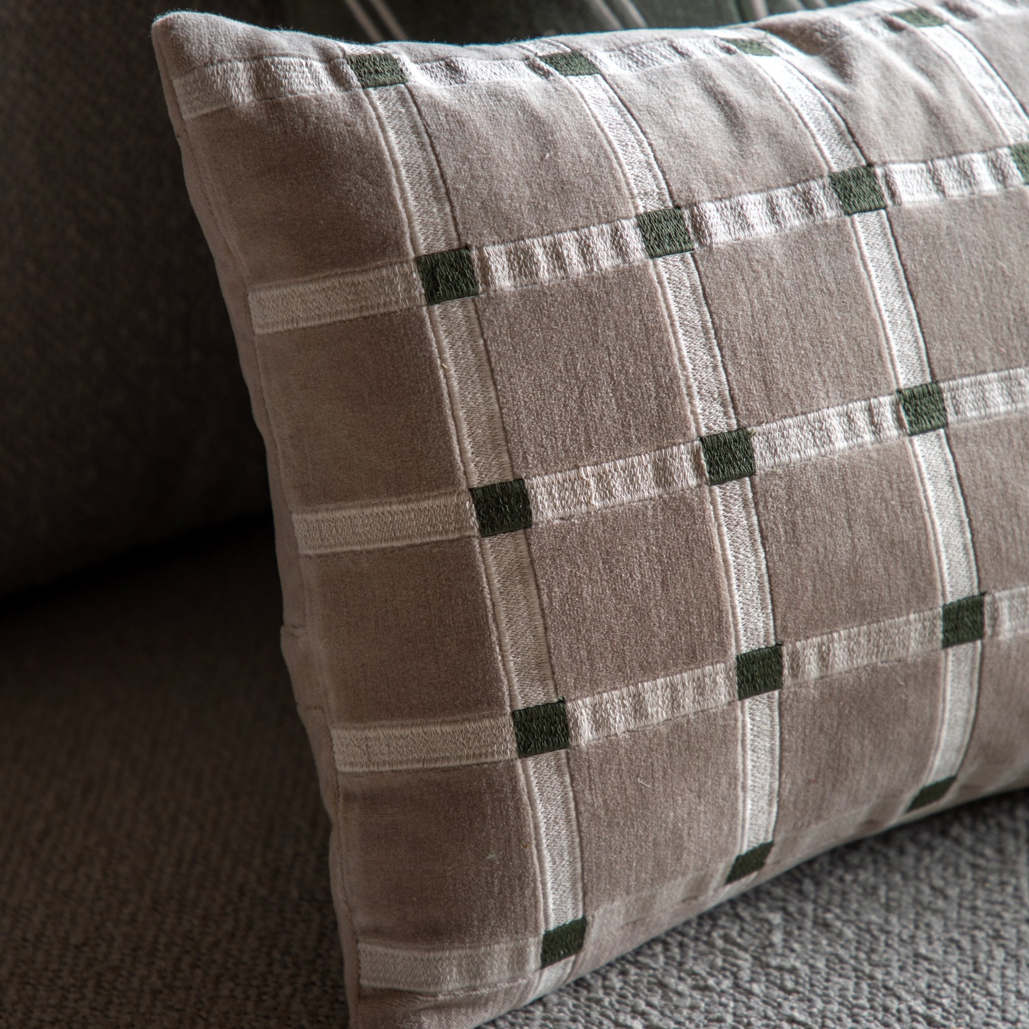 A close-up of a beige and white plaid throw pillow with green accents on a gray sofa.