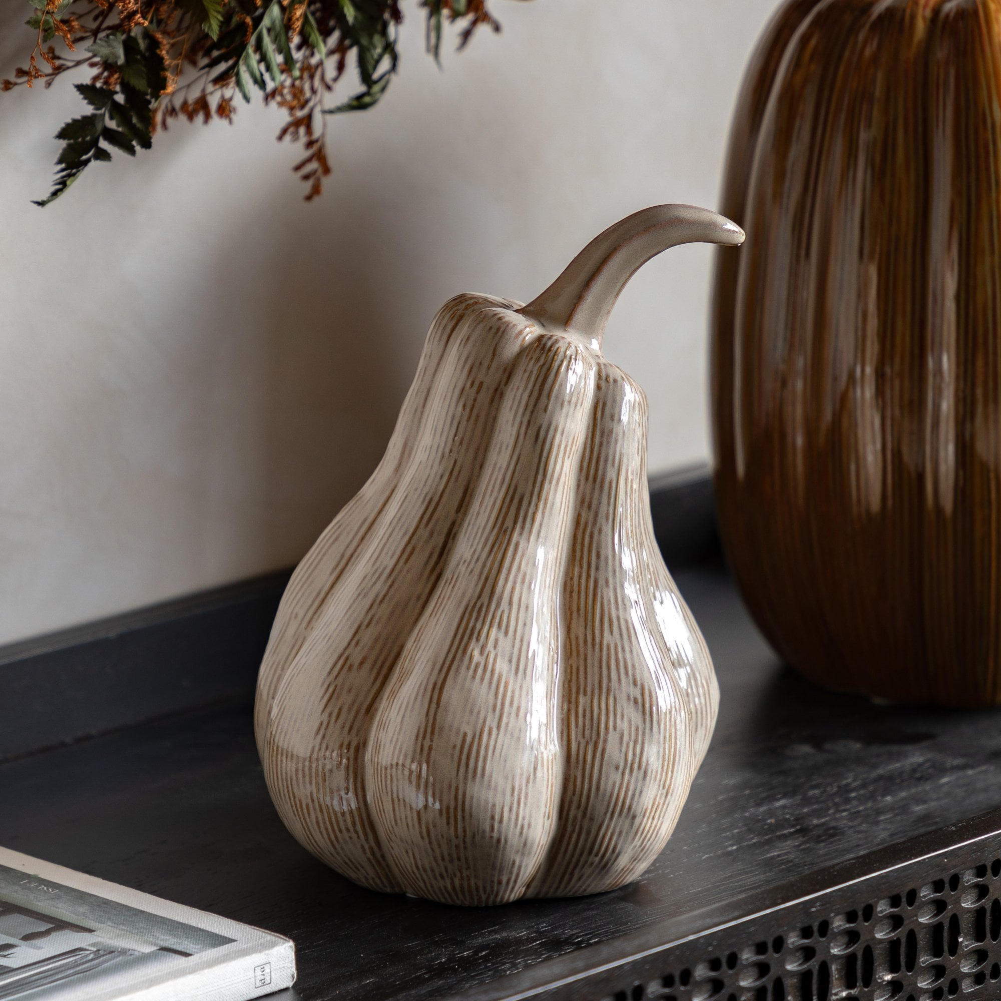 A beige ceramic gourd, with subtle vertical ridges and a curved stem, on a dark wooden surface.