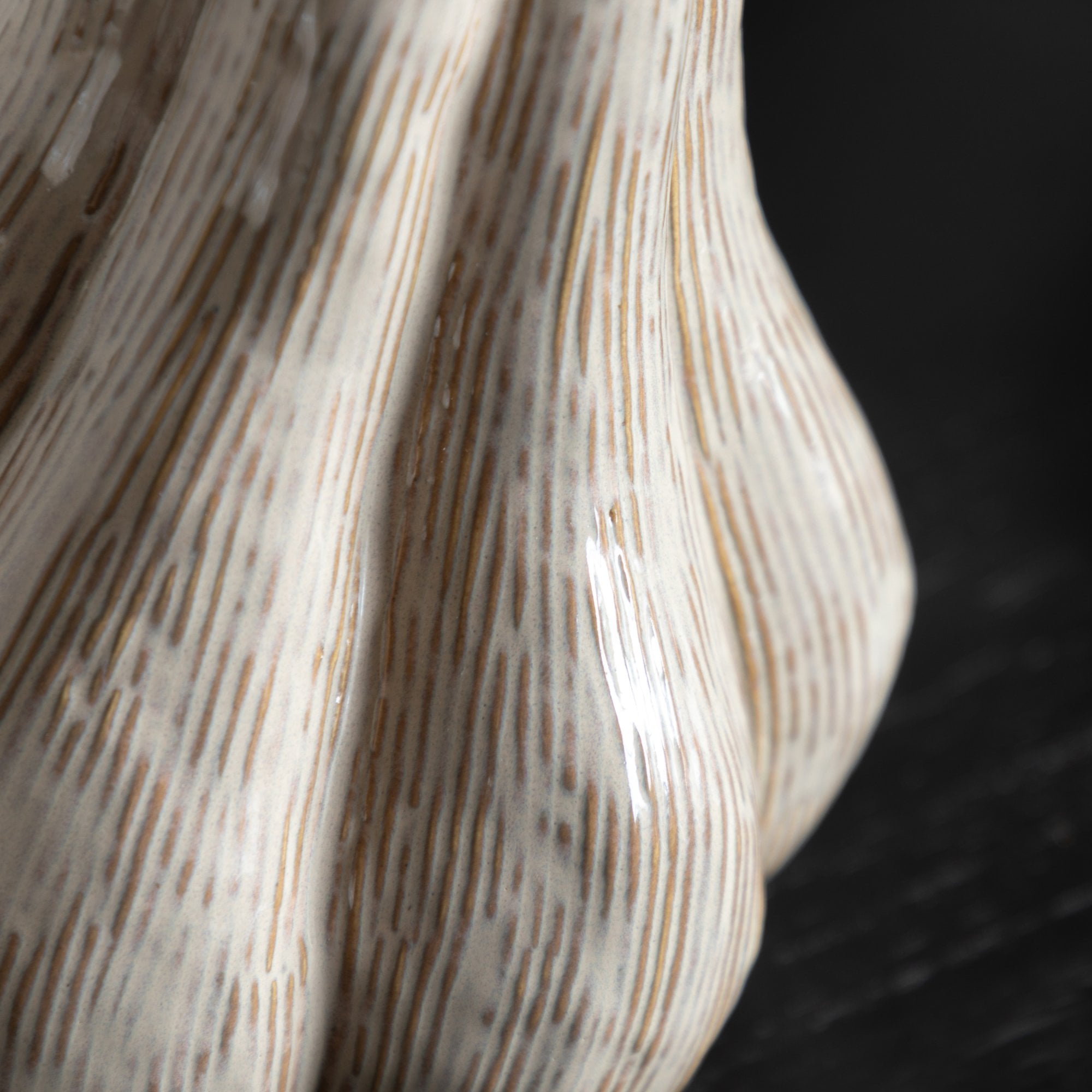 Close-up of the ribbed texture and glossy finish of a light beige ceramic gourd.