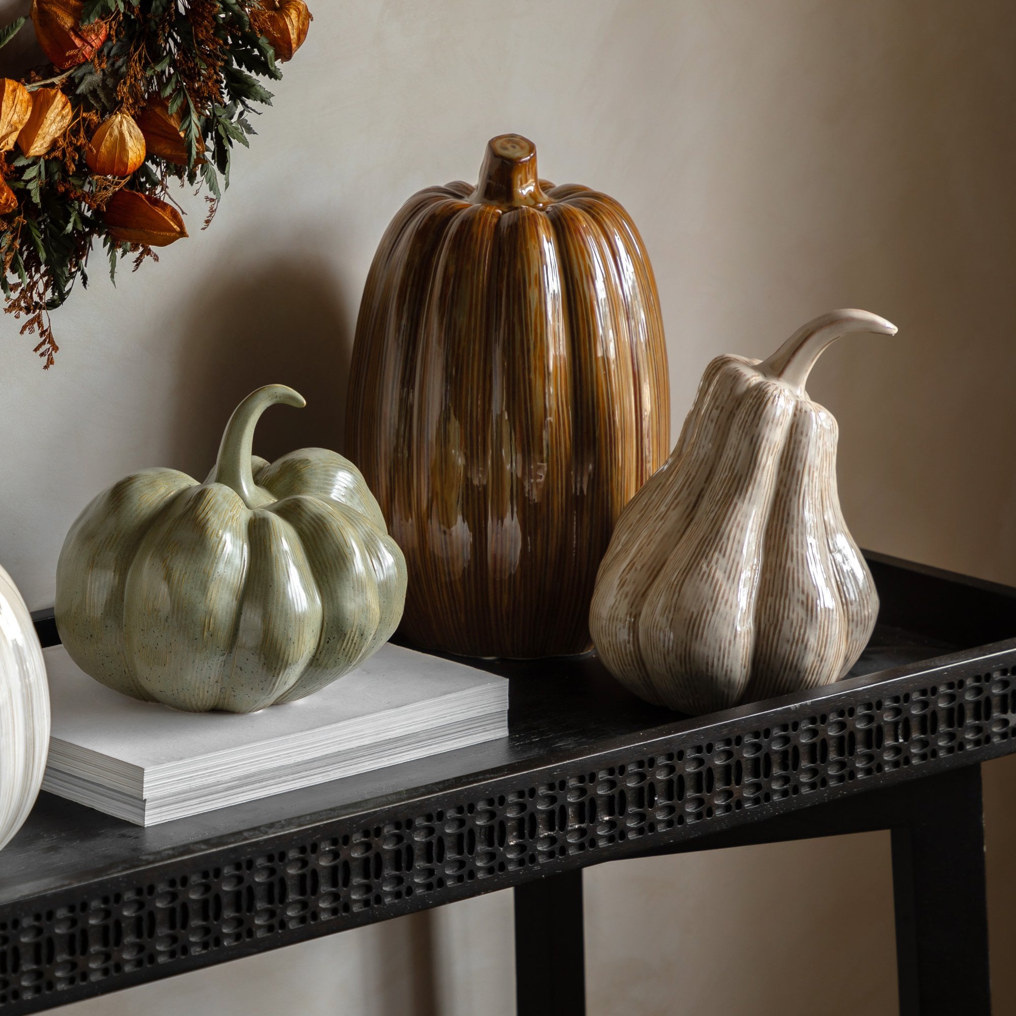 Three ceramic gourds in varying sizes and colors, on a dark console table.