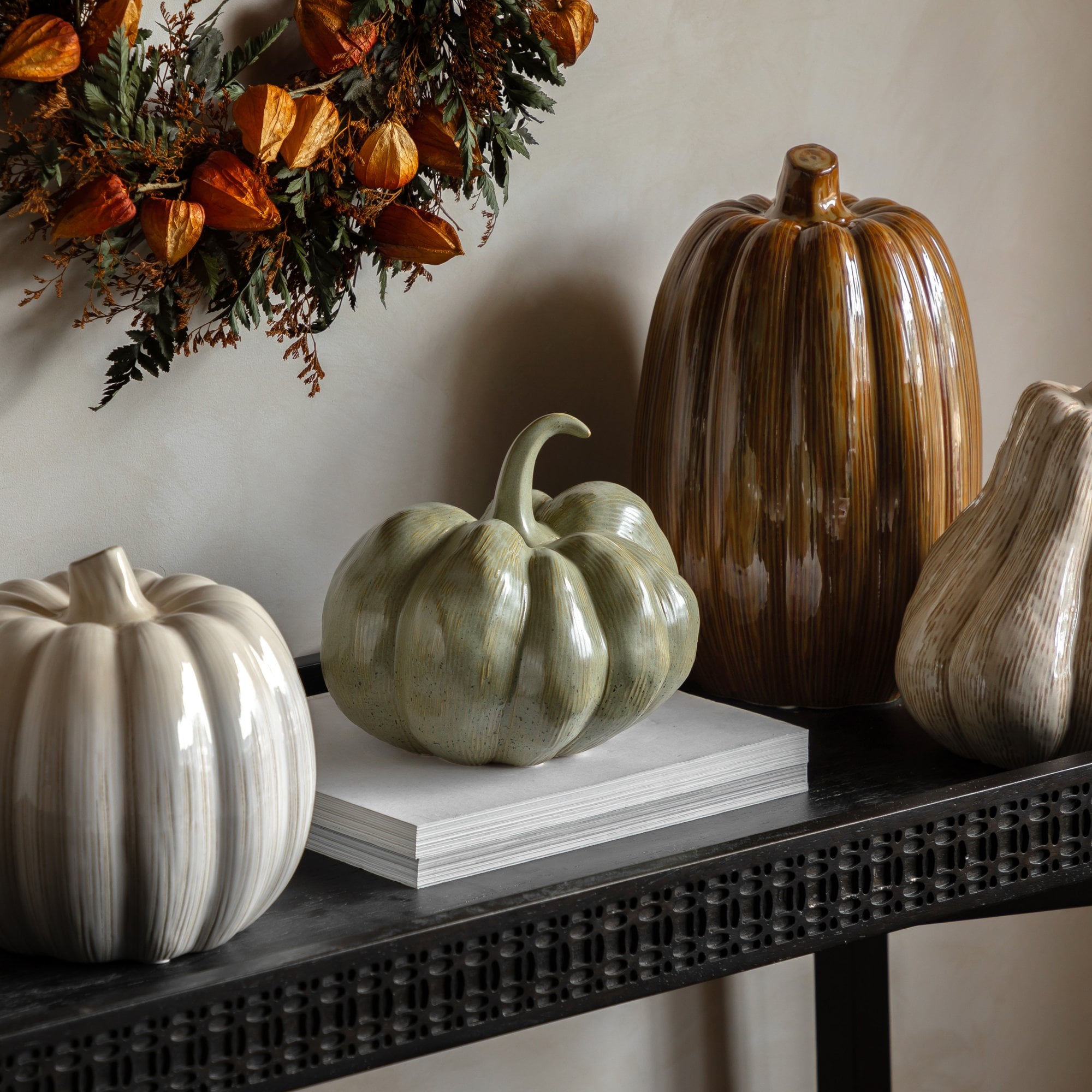 Various ceramic pumpkins on a table with a wreath in the background.