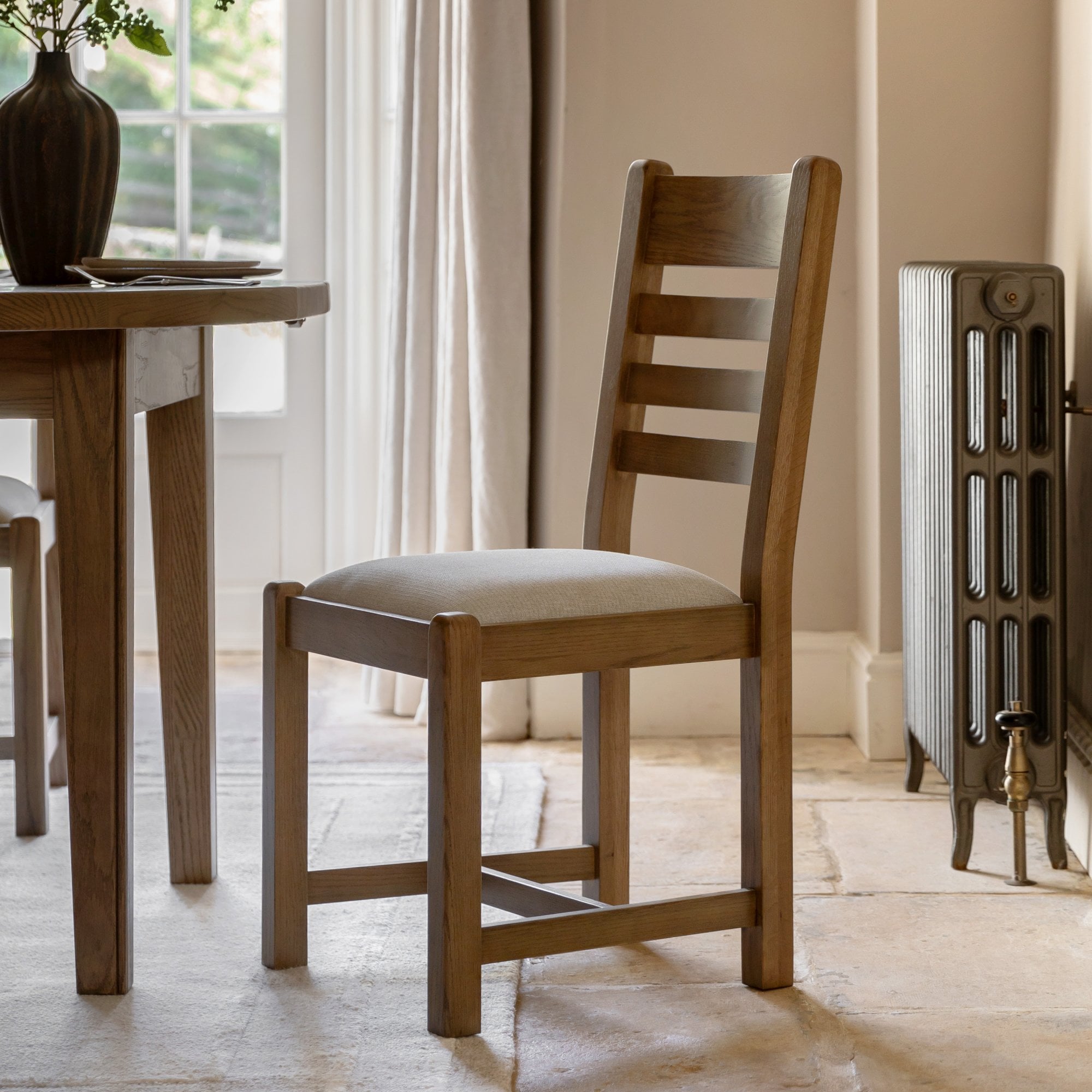 Oak dining chair with a cream upholstered seat in a dining room setting.