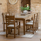 Oak dining table and chairs in a rustic dining room with stone walls.