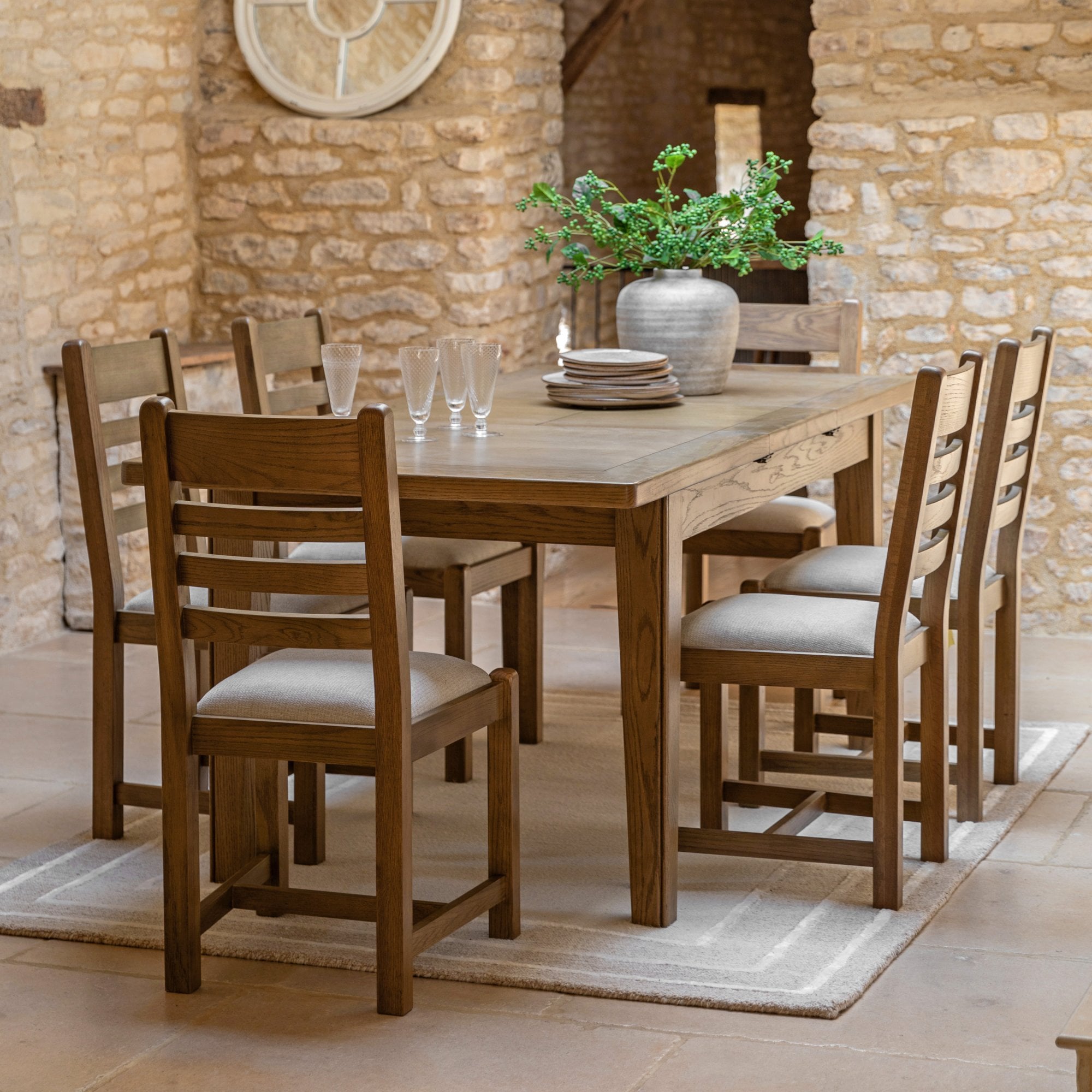 Oak dining table and chairs in a rustic dining room with stone walls.