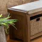 A close-up of the wooden storage bench with a wicker basket and a plant beside it.